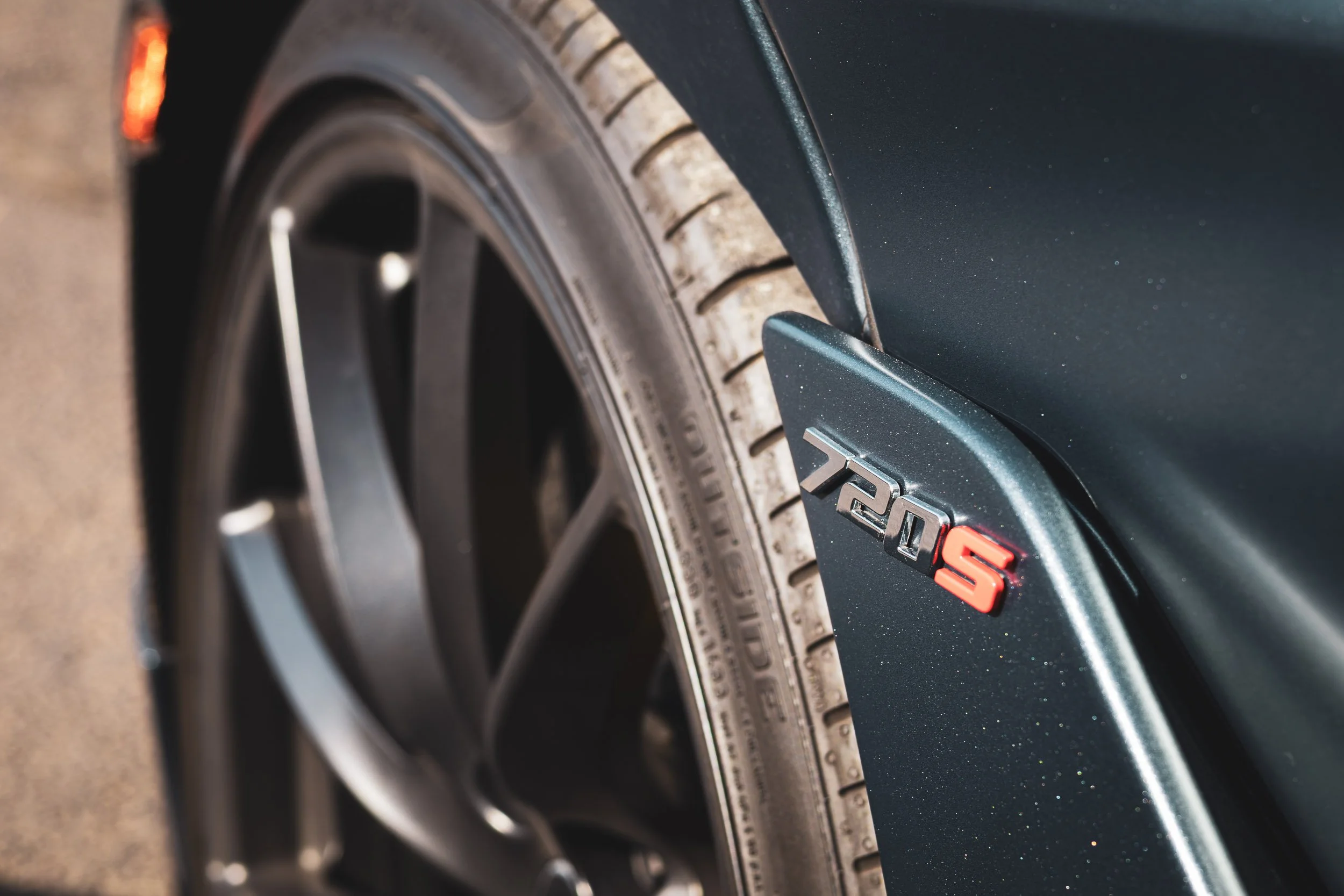 Macro detail car photography highlighting the chrome 720S badge, dark metallic paint, and front wheel fitment of a McLaren supercar in Gilbert, Arizona, captured by Curtis from Gasoline and Dopamine.