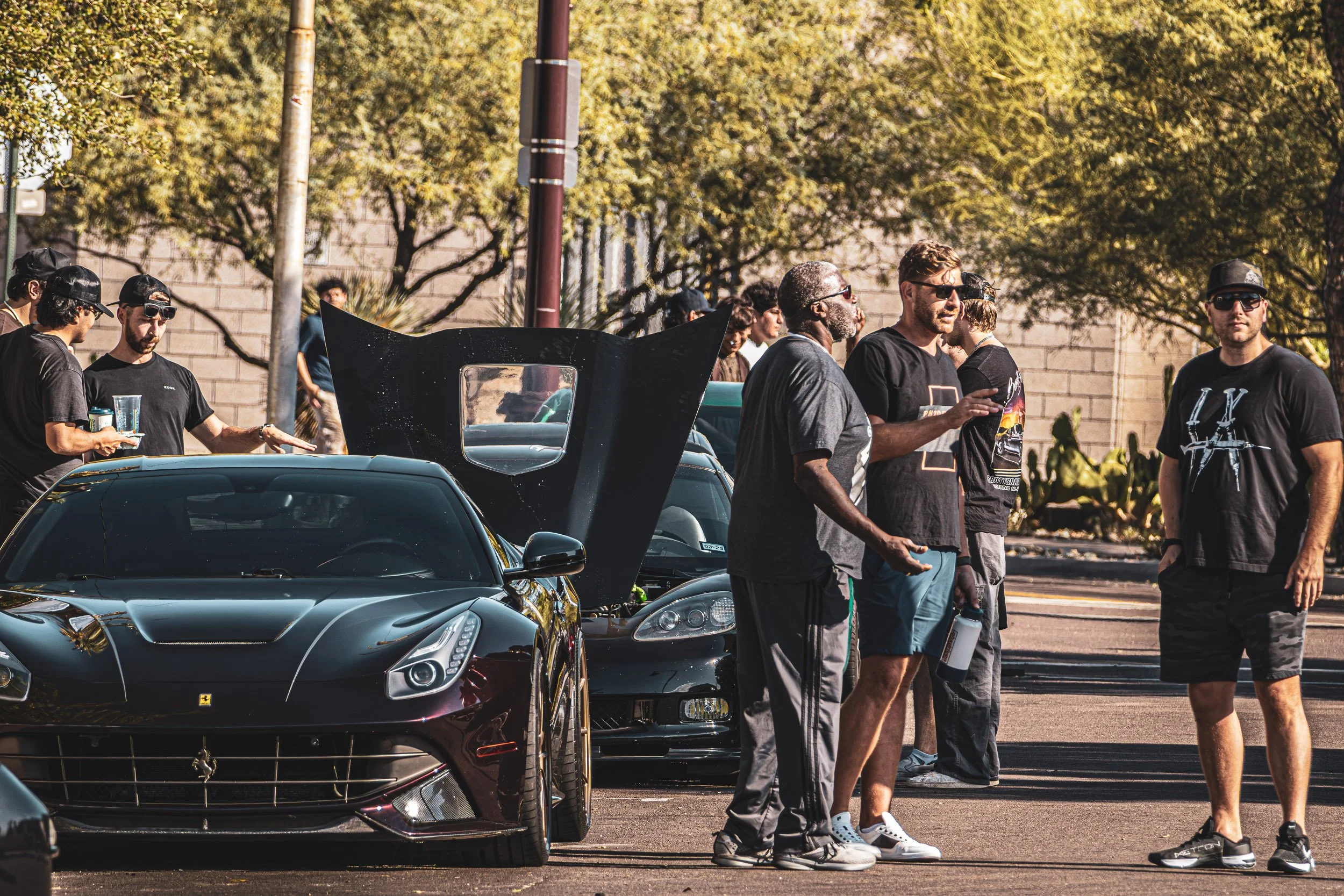 A candid shot of Arizona car culture featuring a group of enthusiasts admiring a dark red Ferrari F12 Berlinetta at a morning cars and coffee event, captured in Scottsdale by Curtis from Gasoline and Dopamine.