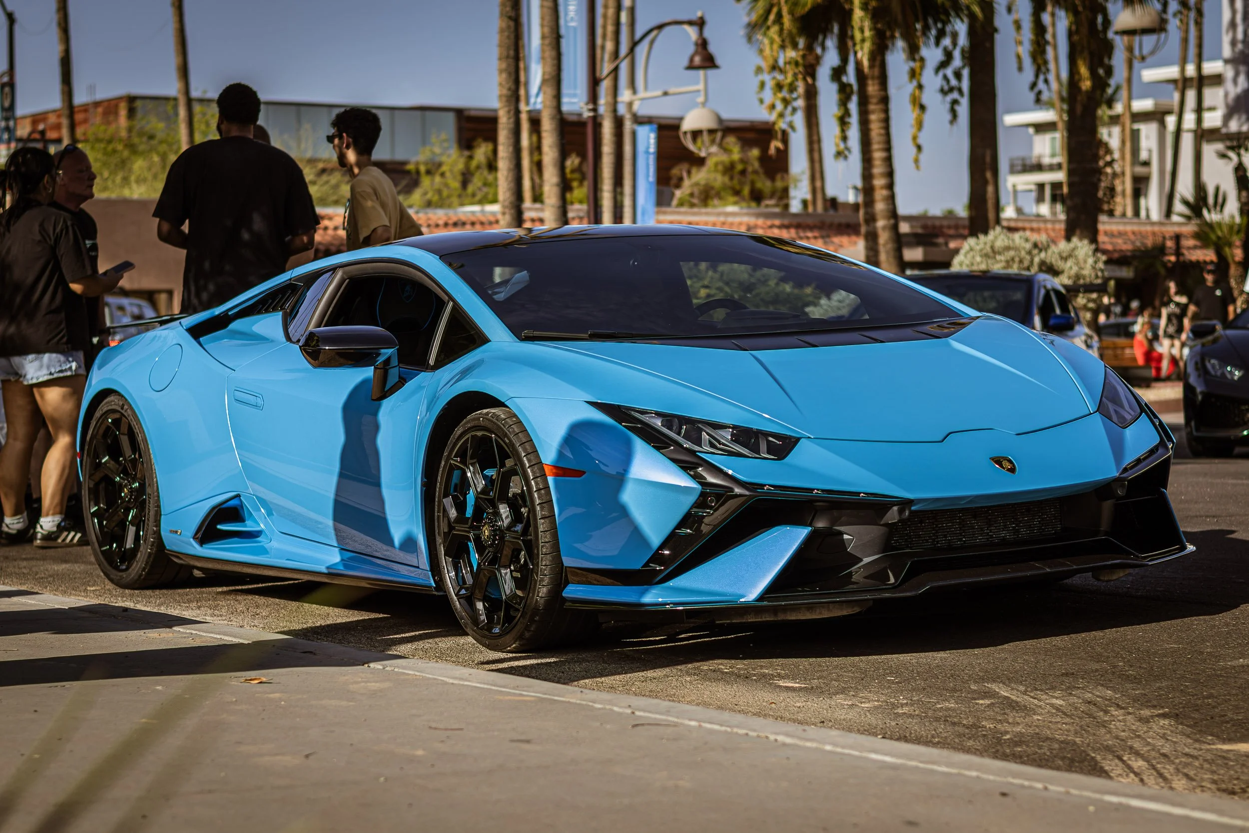 Exotic car photography capturing a low front-quarter angle of a vibrant baby blue Lamborghini Aventador Ultimae parked on a sunny street during a cars and coffee event in Scottsdale, Arizona, shot by Curtis from Gasoline and Dopamine.