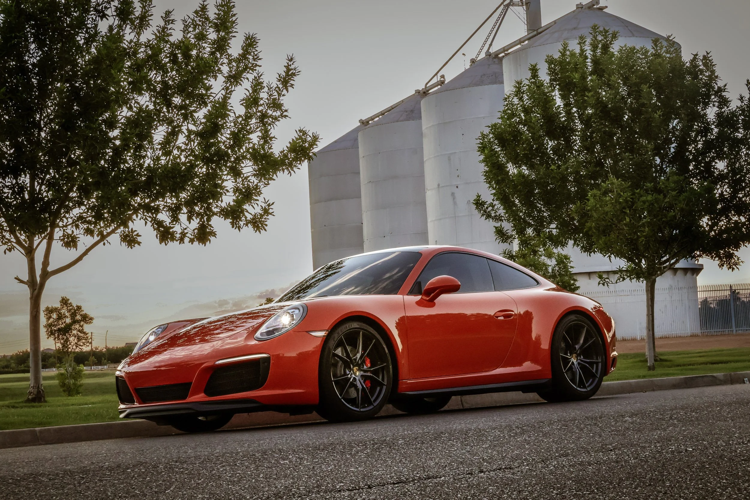 Sunset automotive photography featuring a vibrant Lava Orange Porsche 911 C4S parked in front of the historic Morrison Ranch silos in Gilbert, Arizona, captured by Gasoline and Dopamine.