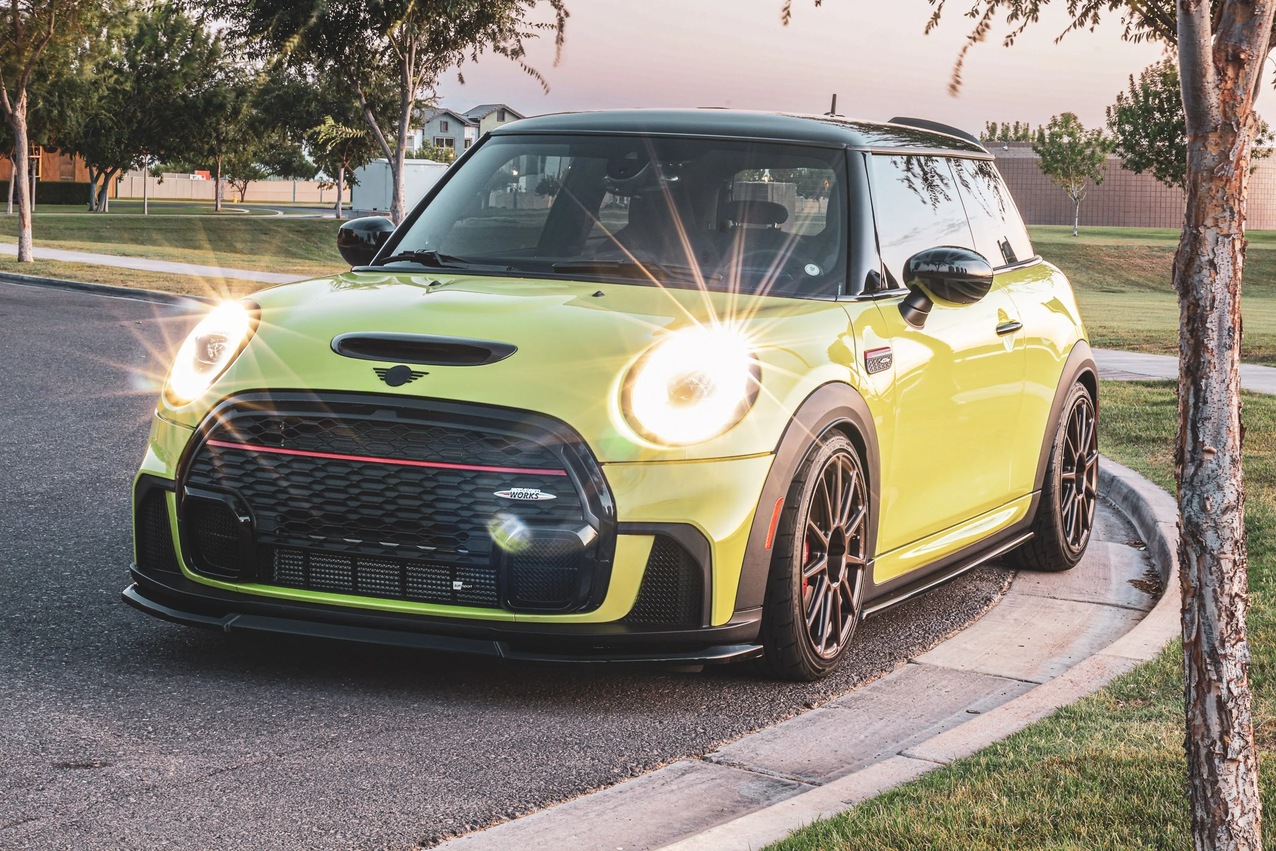 Low-angle automotive photography showcasing a vibrant yellow Mini Cooper JCW with brightly illuminated halo headlights, parked on a street corner near sunset in Morrison Ranch, Gilbert, Arizona, captured by Gasoline and Dopamine.