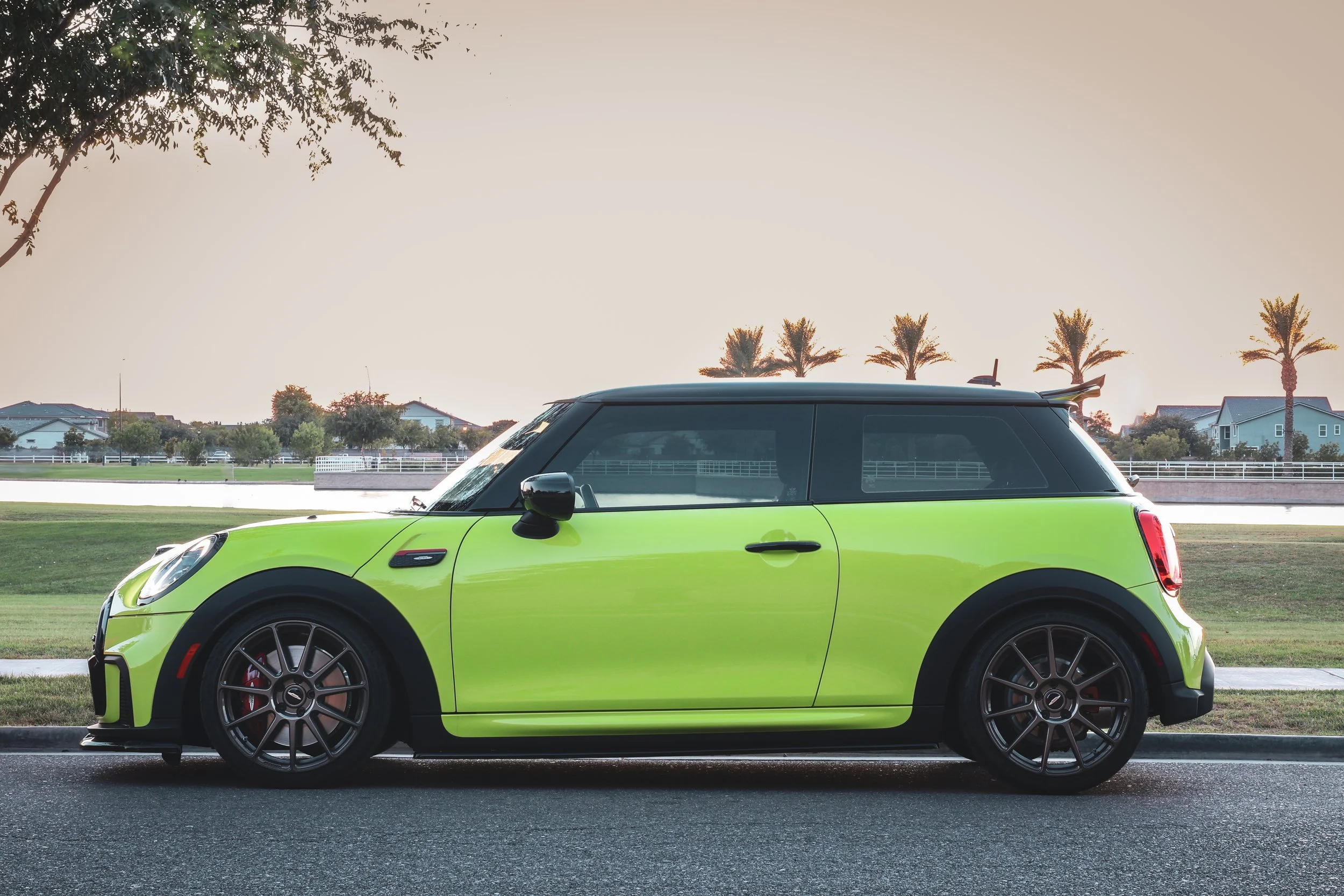 A wide angle side-view of a Zesty Yellow Mini Cooper John Cooper Works parked on a street under a tree near the iconic Morrison Ranch Silos in Gilbert, AZ.