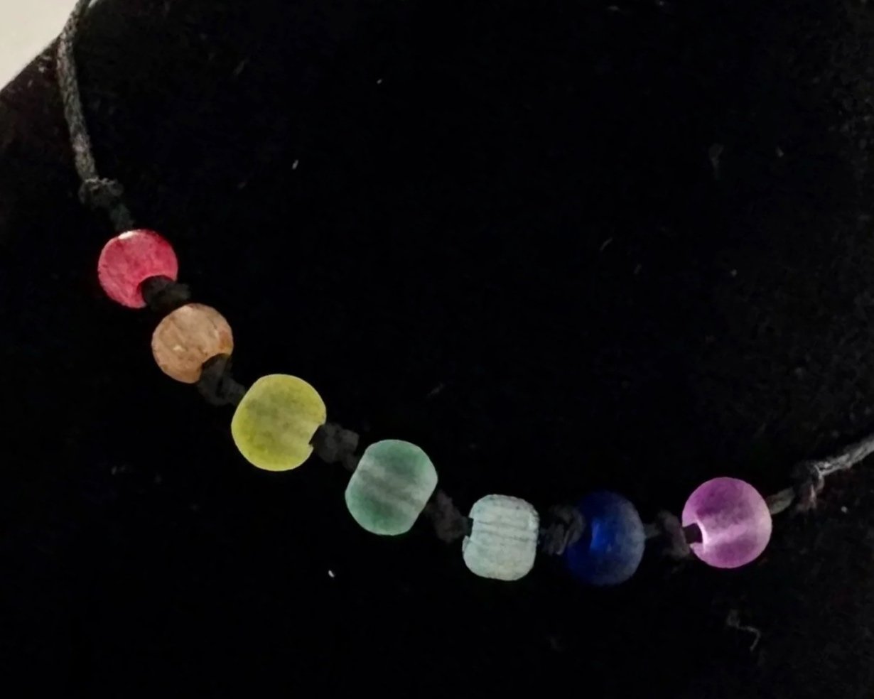 Colorful beaded bracelet with round beads in red, yellow orange green, blue, indigo , and violet on a black background. Reminders of God's promises