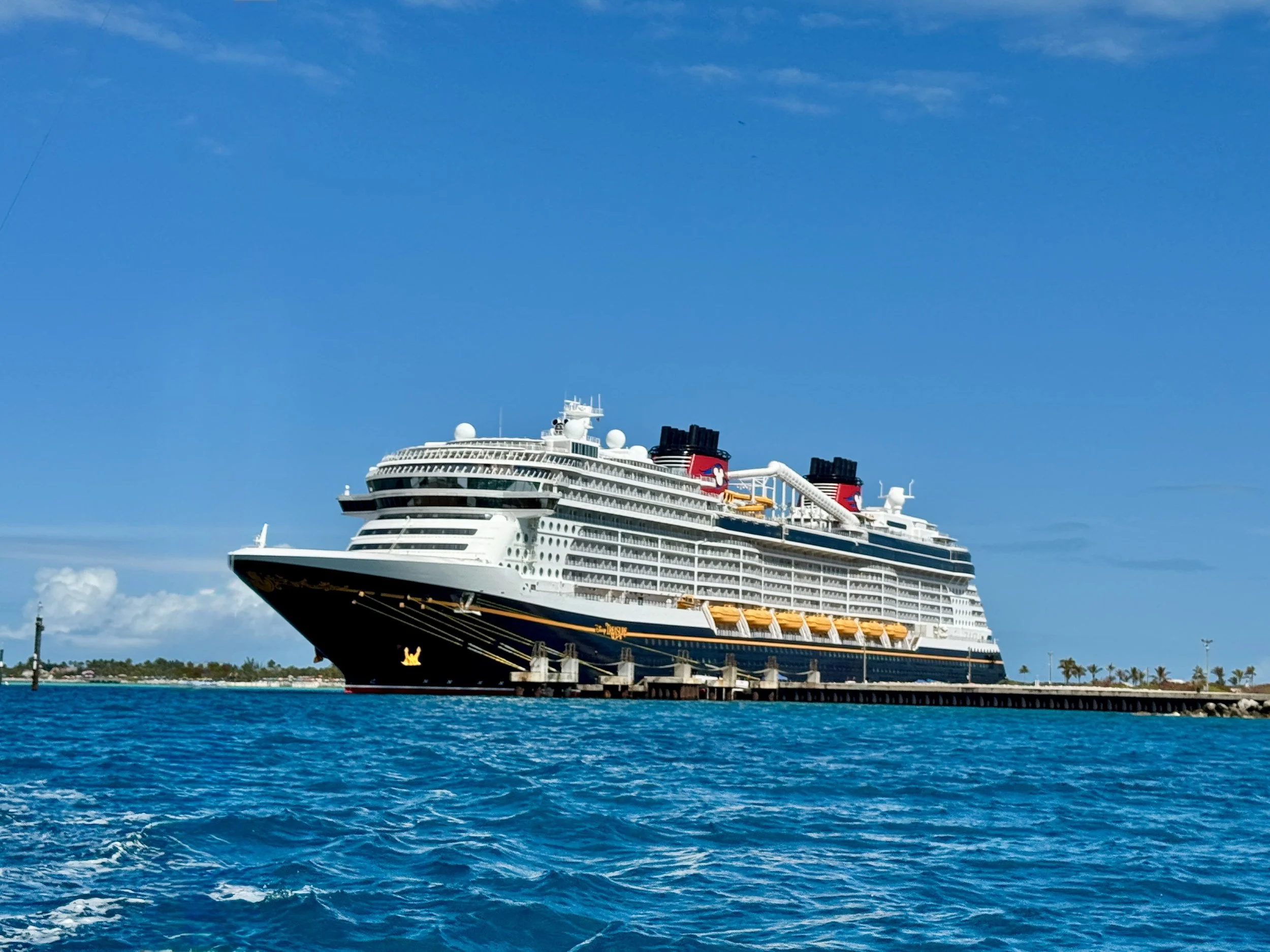 Large cruise ship docked in a harbor with clear blue water and a bright blue sky.