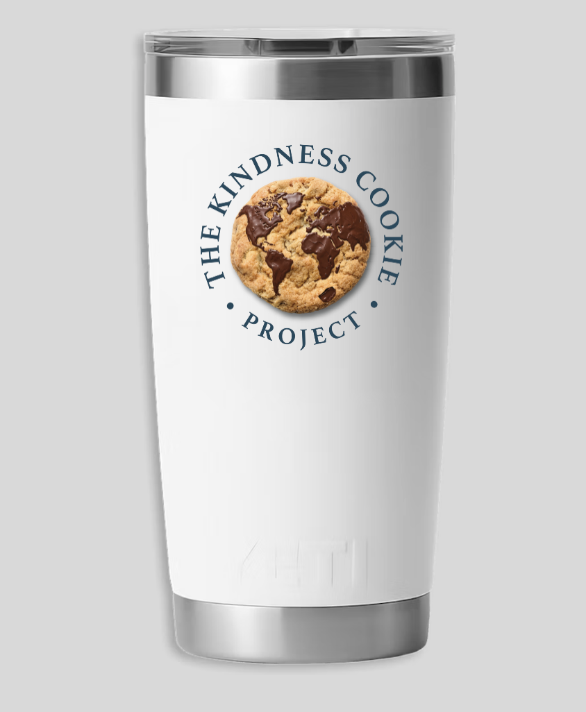 A white tumbler with a silver lid and bottom, featuring a logo of a cookie with a world map design and the text 'The Kindness Cookie Project' encircling it.