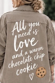 Back of a person wearing a khaki jacket with white cursive text that reads 'All you need is love and a warm chocolate chip cookie' and a small illustration of a cookie