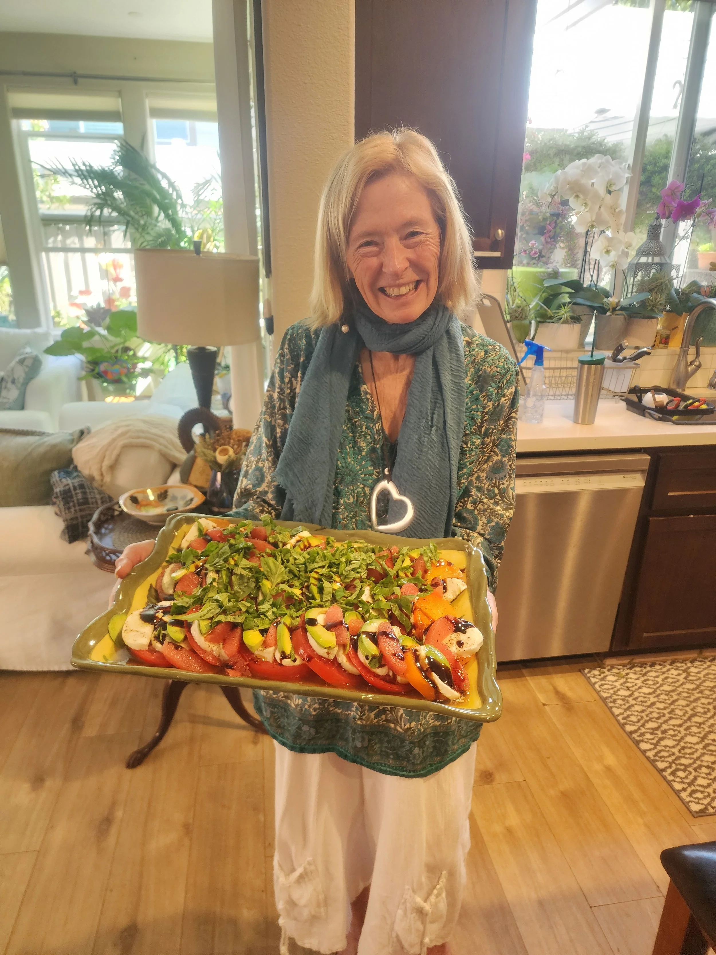 A person holding a large platter of salad with various vegetables and dressings in a kitchen.
