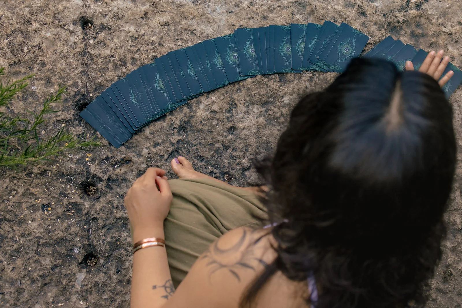 A person sitting on dirt ground with tarot cards laid out in a semi-circle in front of them, seen from above.