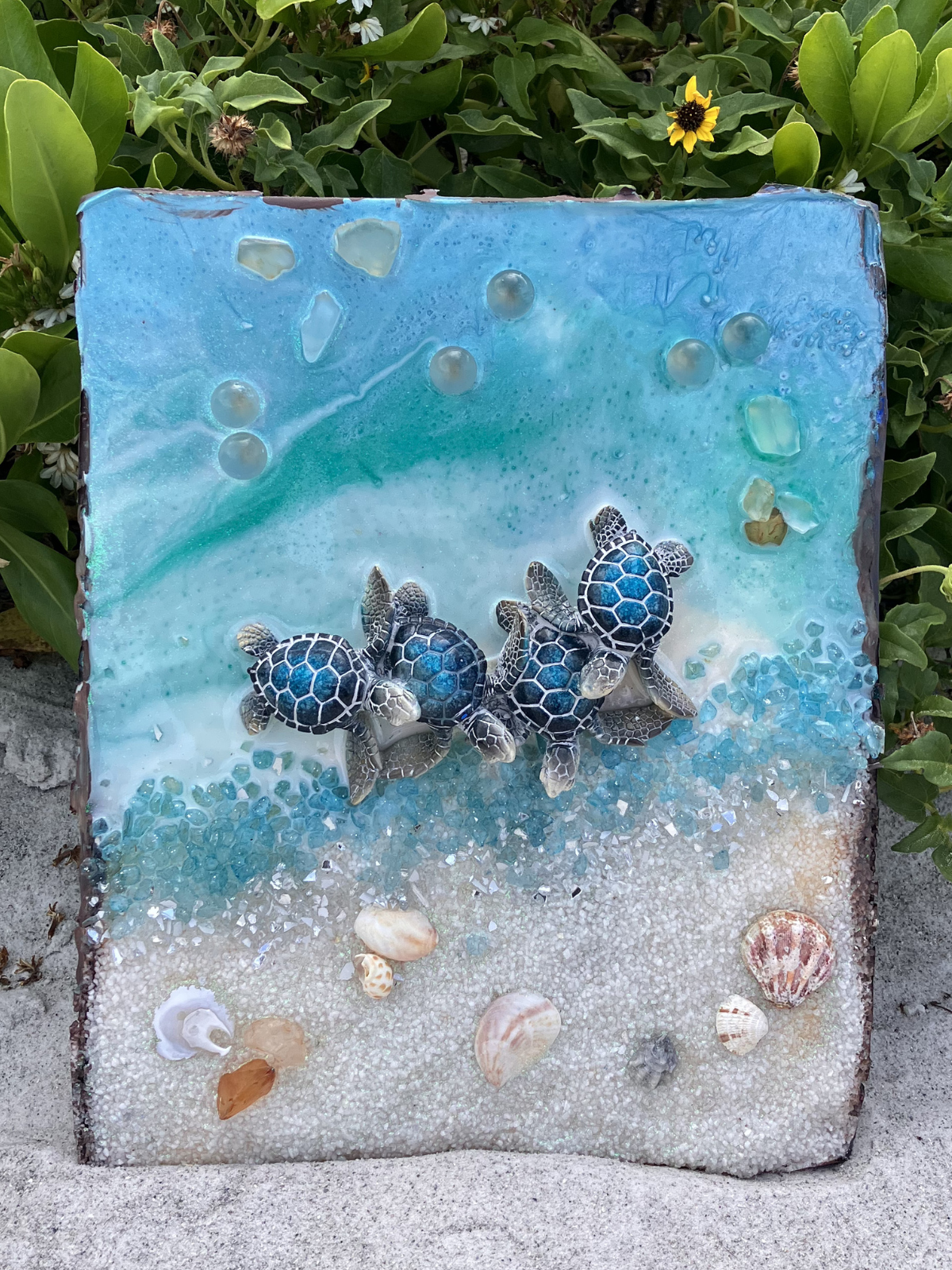 A decorative glass art piece featuring a beach scene with five small sea turtles, seashells, and blue ocean elements.
