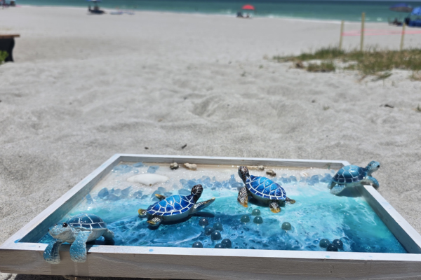 A pinball machine with turtle figurines and colorful marbles on a sandy beach.