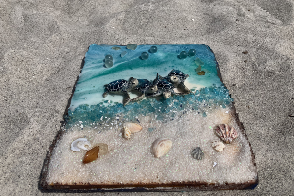 A small decorative beach scene with tiny turtles, seashells, and blue glass beads on a textured surface.