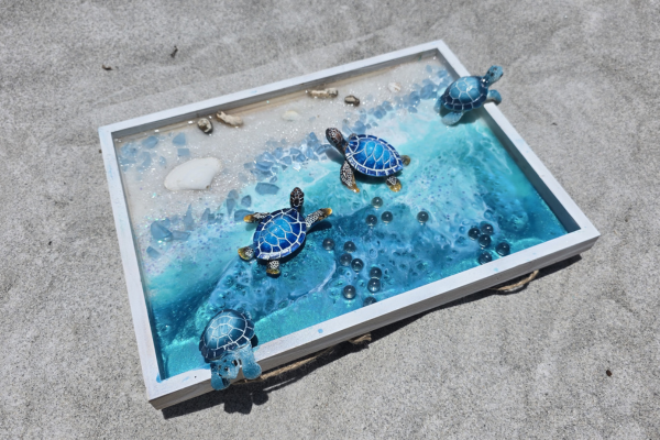 Decorative tabletop with small turtle figurines, blue water, and stones, on a concrete surface.