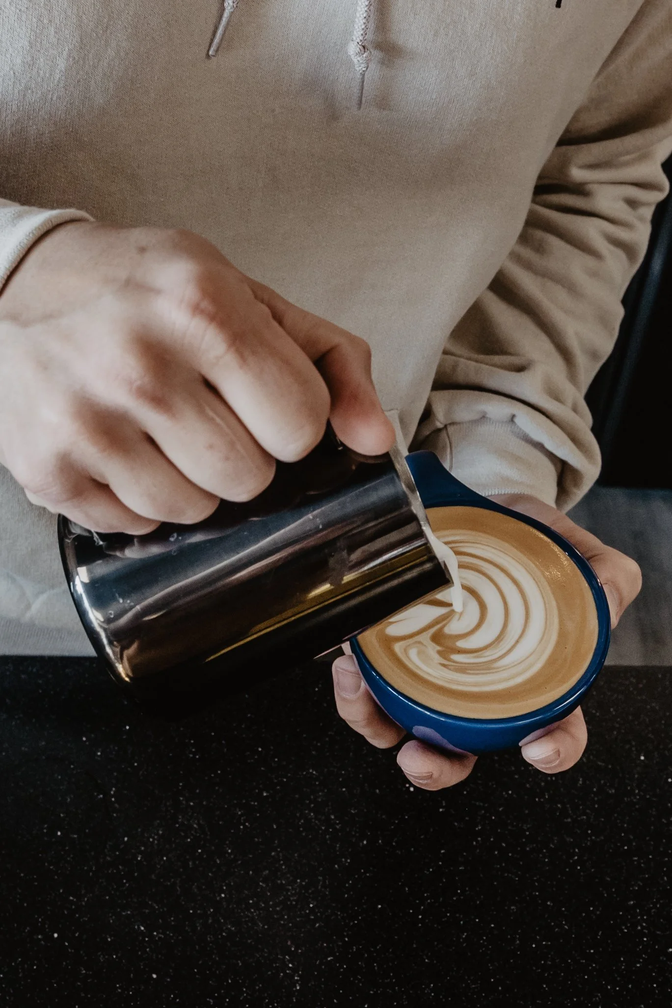 Person pouring steamed milk into a coffee cup to make latte art.