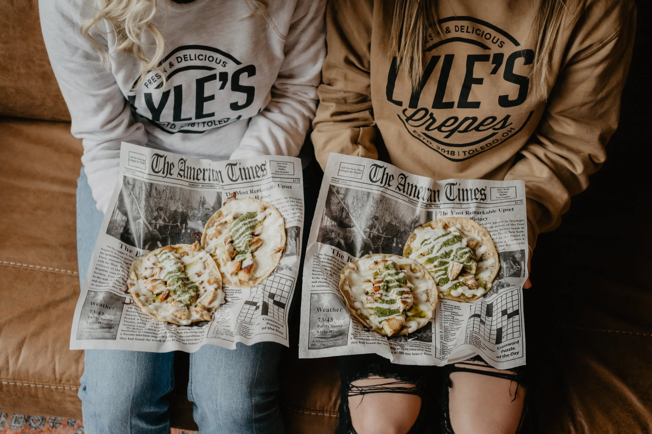 Two people sitting on a brown couch, wearing sweatshirts with 