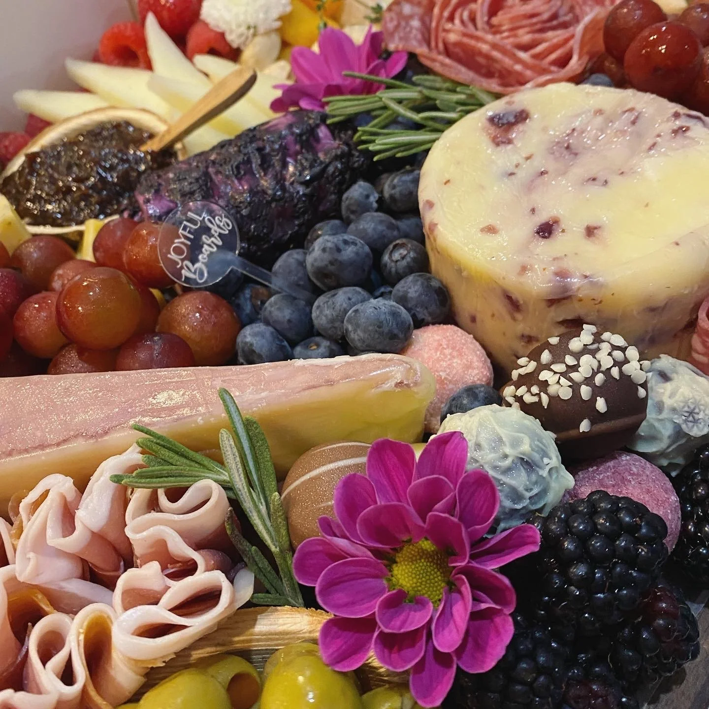 Assorted cheeses, fresh blueberries, grapes, cured meats, and flowers in a gourmet platter.