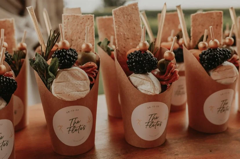 Cups of appetizers with cheeses, blackberries, olives, crackers, and garnishes, labeled 'The Flavors'.