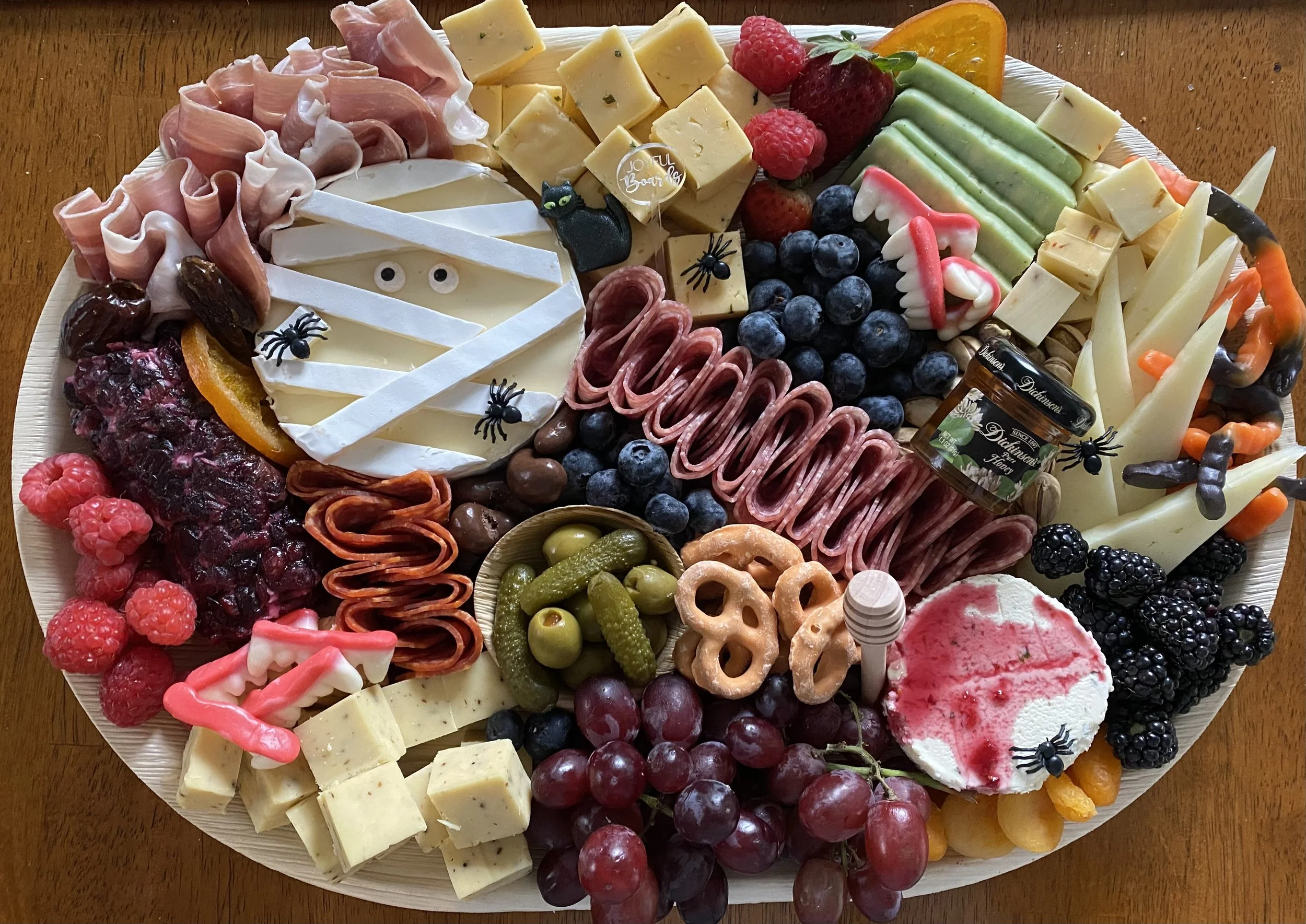 Assorted cheeses, grapes, berries, crackers, and candies arranged on a platter for a Halloween party, with small Halloween decorations.