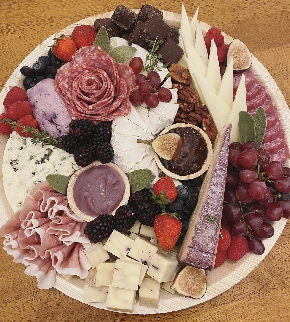 Cheese platter with assorted cheeses, cured meats, fresh berries, figs, nuts, and chocolate.