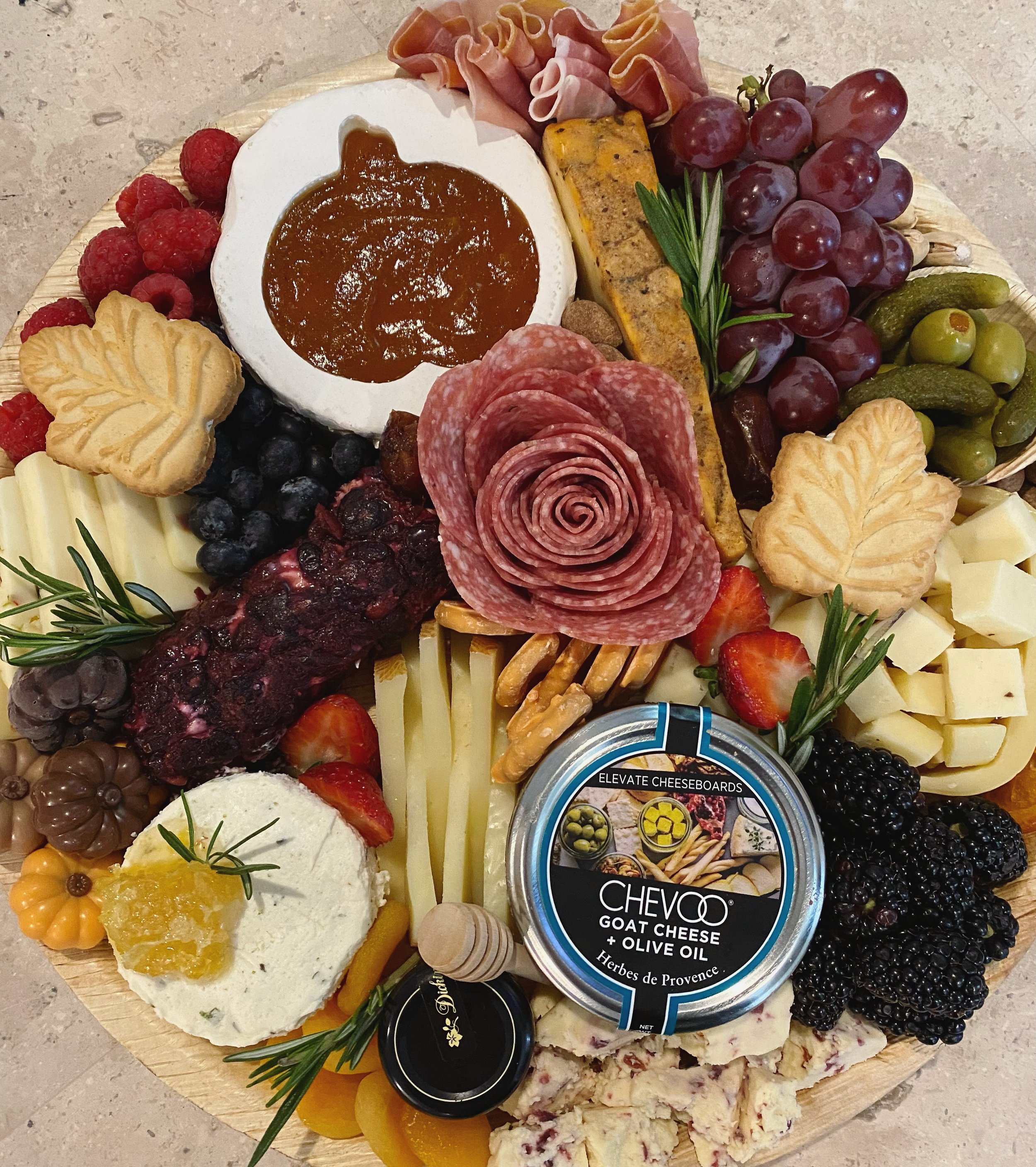Charcuterie board with assorted cheeses, grapes, berries, crackers, sliced meats, olives, and a cheese spread with herbs.