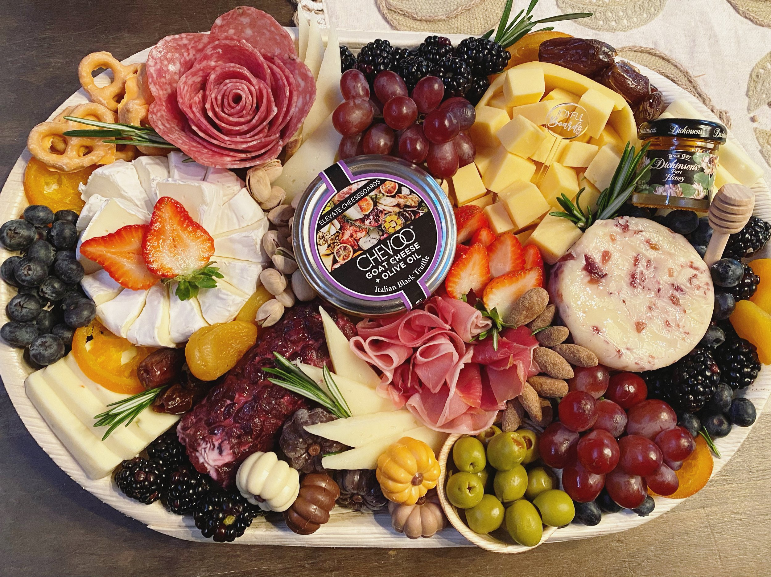 A cheese and fruit platter with grapes, strawberries, blueberries, peaches, and slices of cheese and cured meats, garnished with herbs and nuts.