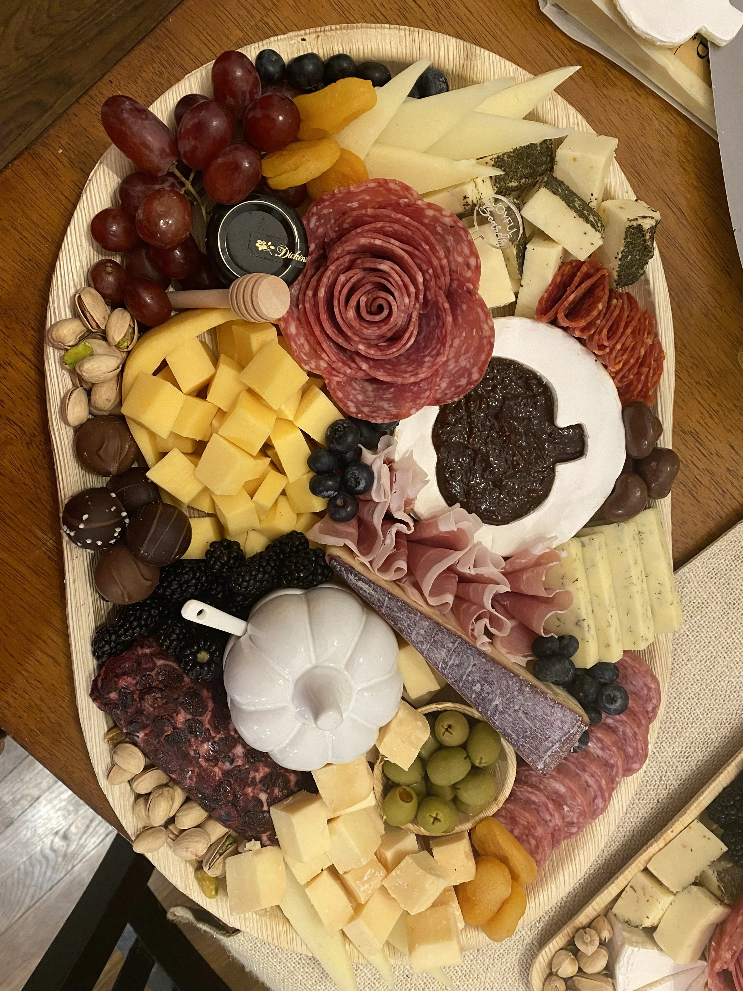 A cheese and charcuterie platter with different cheeses, grapes, dried fruits, meats, nuts, and spreads on a wooden table.