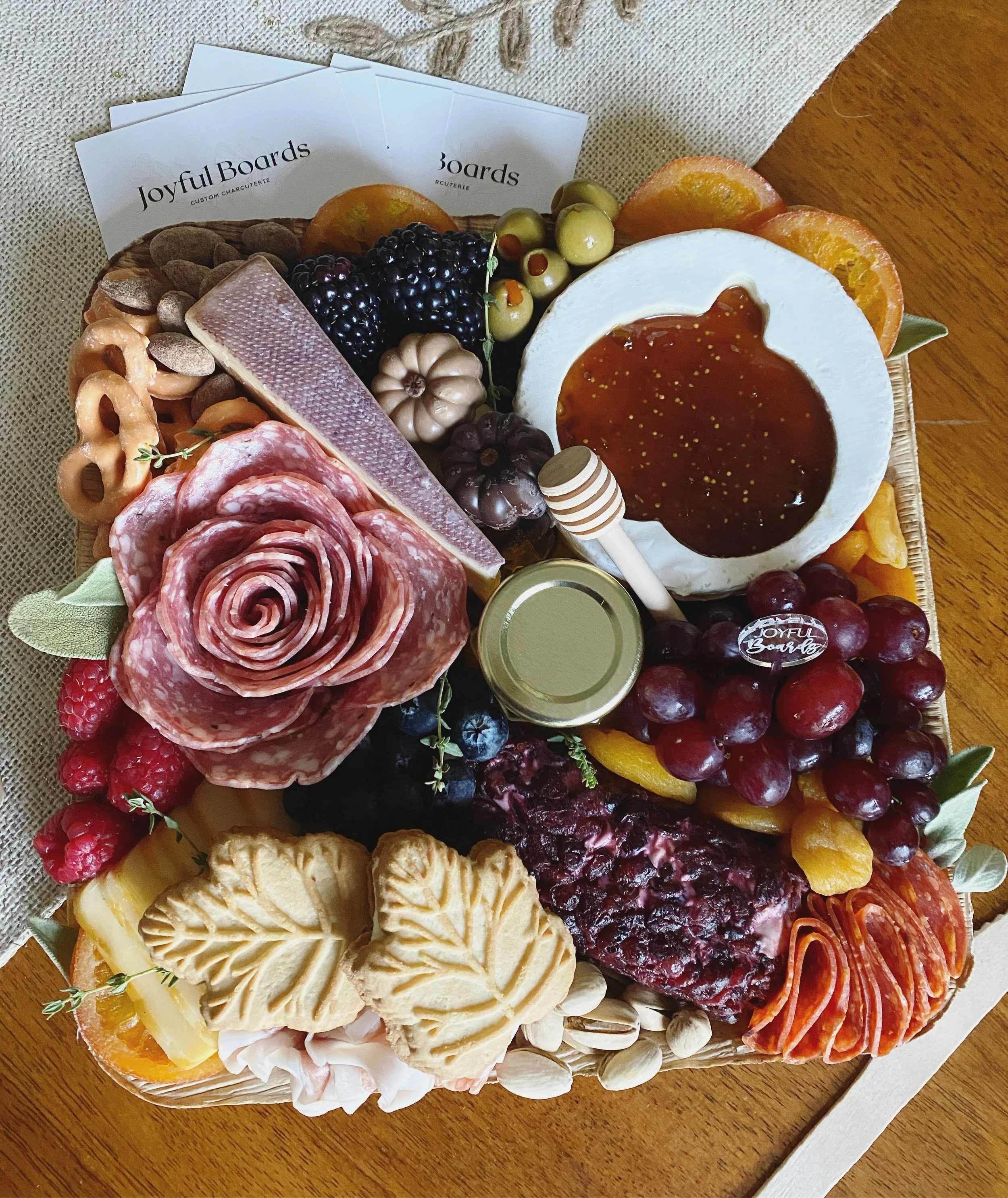 A platter of assorted cheeses, fruits, and charcuterie including slices of orange, grapes, berries, sliced salami, and assorted cheeses on a wooden table