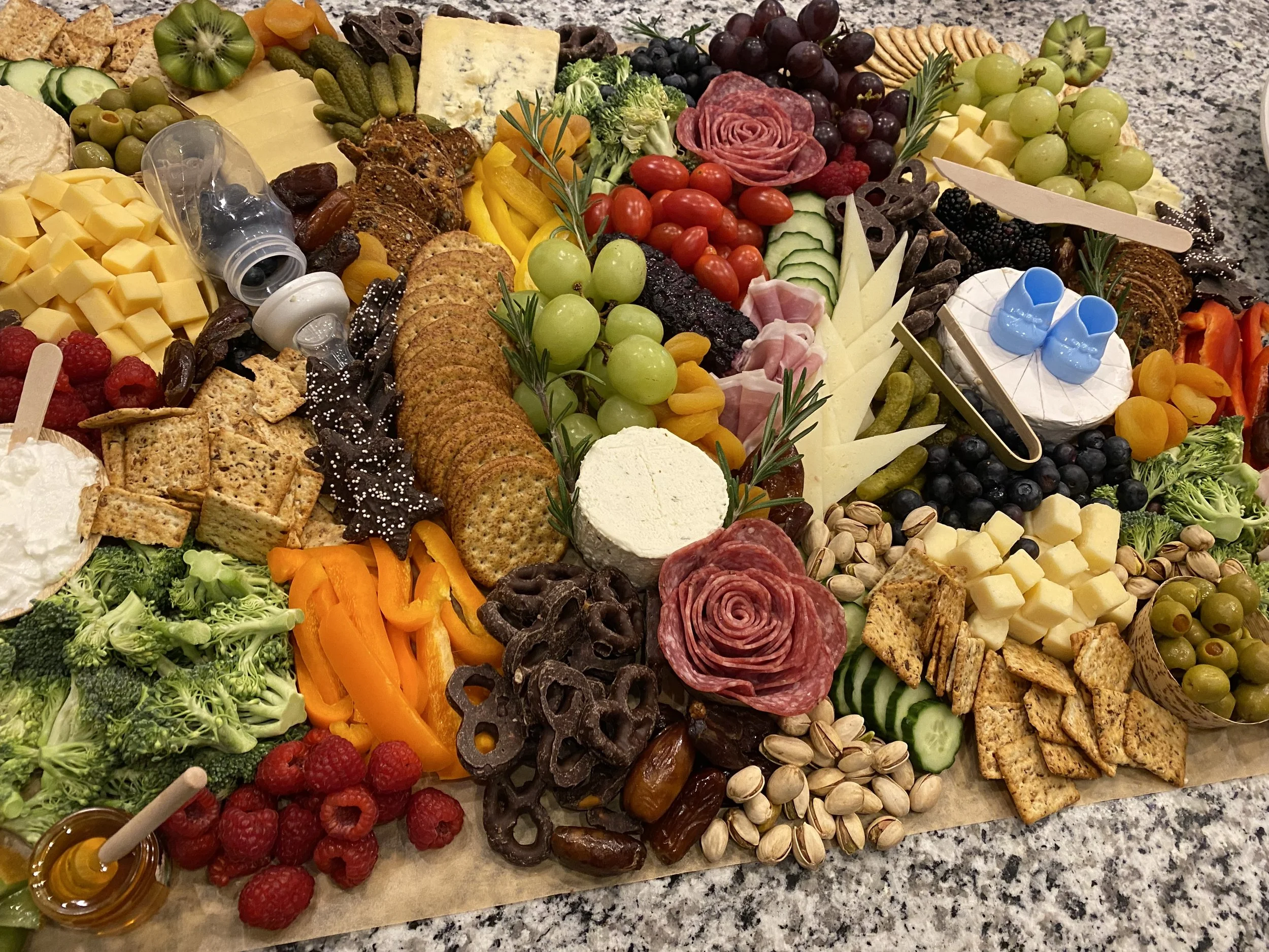 A large platter with a variety of foods including cheese, grapes, cherry tomatoes, cucumber slices, crackers, smoked meats, blackberries, raspberries, nuts, and vegetable slices. There are crackers, cheeses, fruits, vegetables, and assorted snacks ar