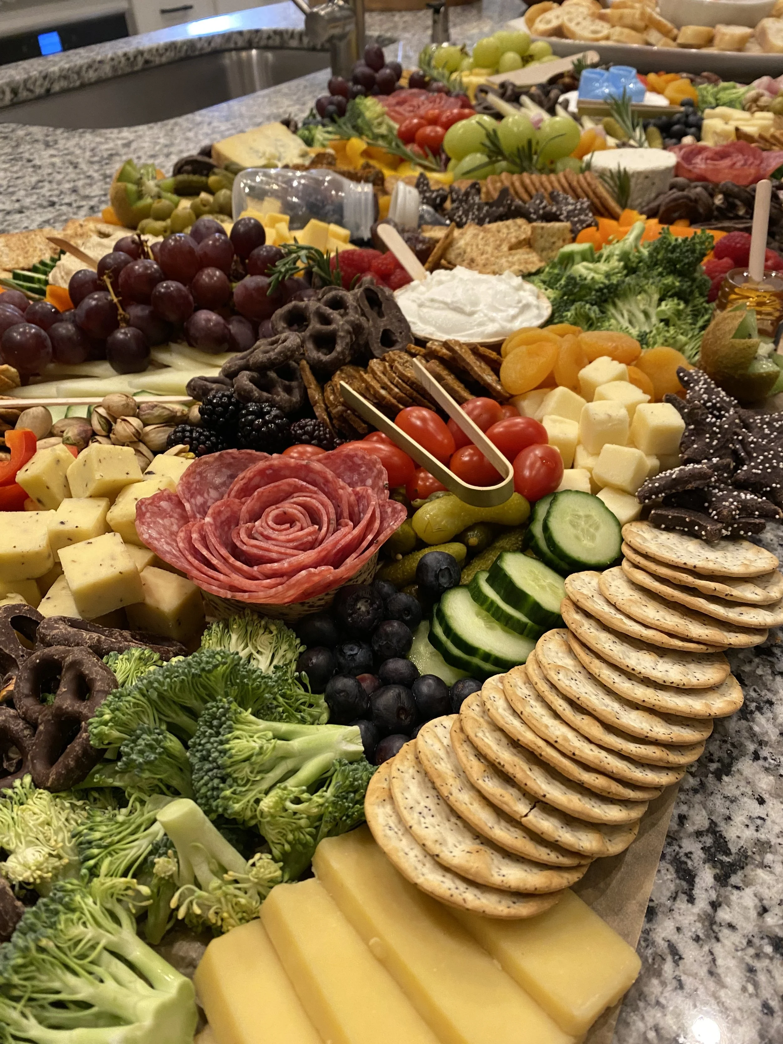 A large spread of cheese, crackers, fresh fruits, vegetables, cured meats, and snacks arranged on a countertop for a snack platter or charcuterie board.