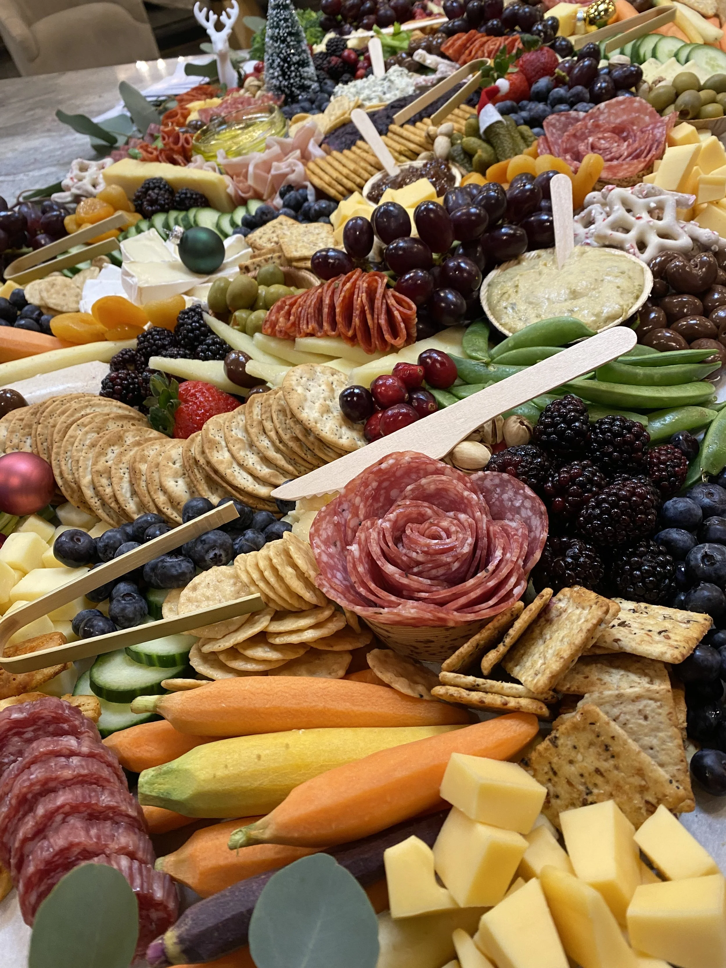 A large cheese and charcuterie board with various cheeses, grapes, sliced meats, crackers, vegetables, and decorative items for a festive setting.