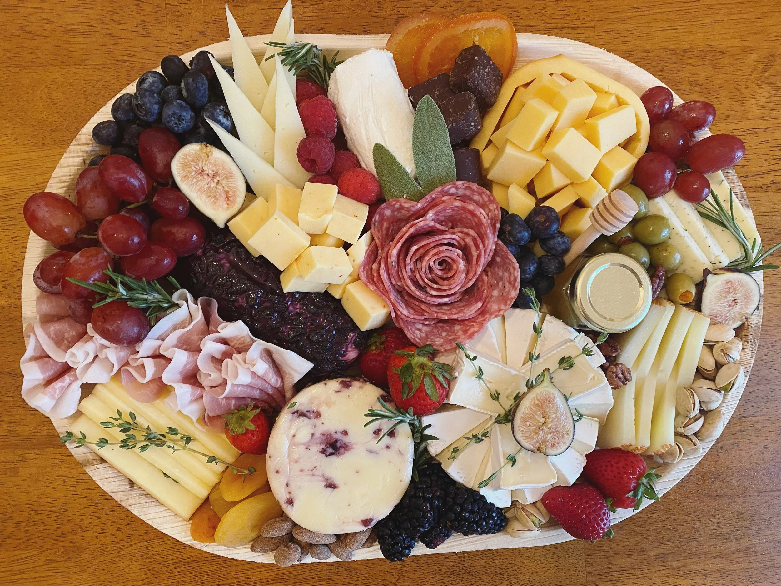 A cheese and charcuterie platter with grapes, strawberries, figs, raspberries, dried apricots, almonds, and various cheeses on a wooden table.