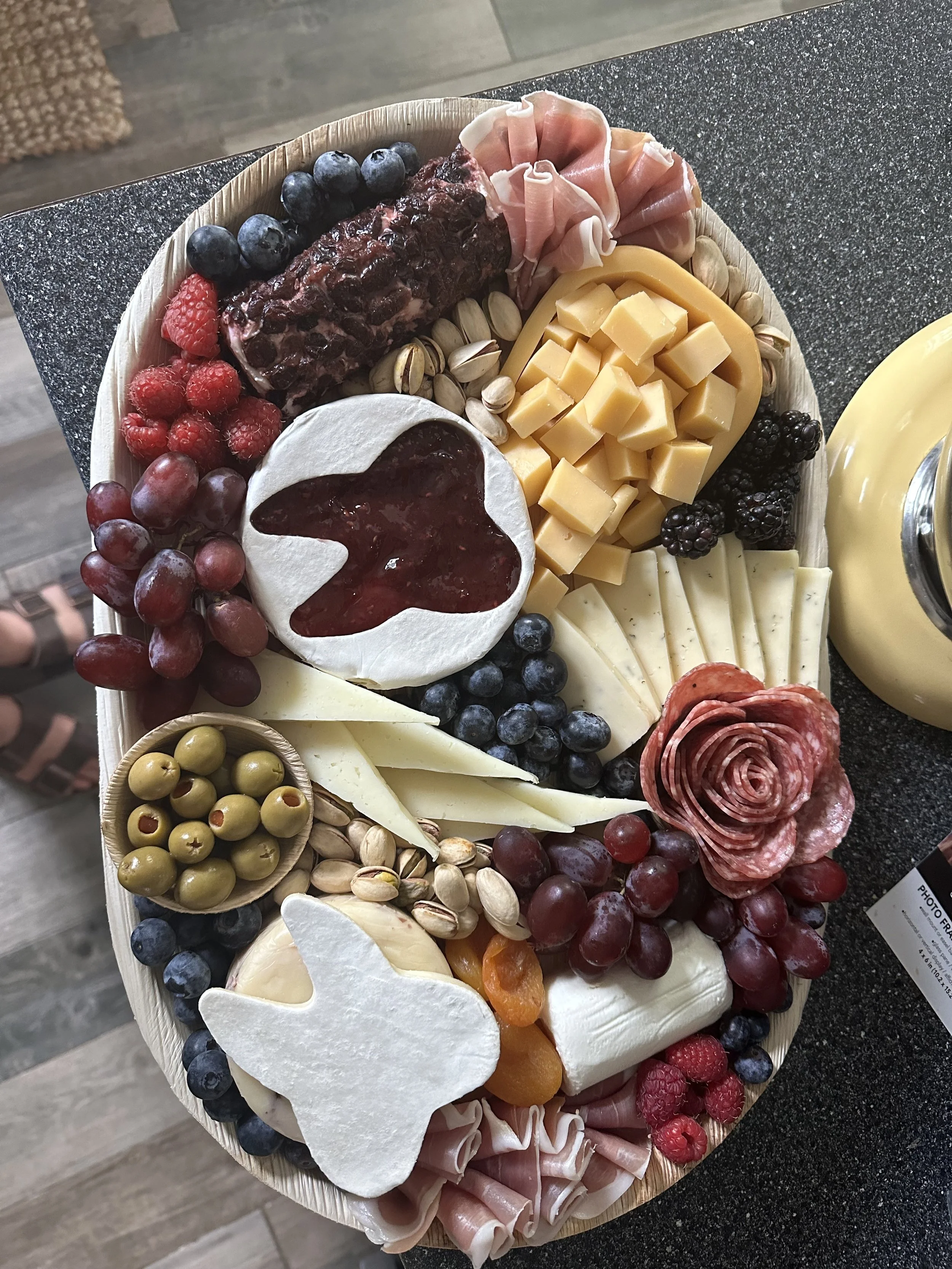 A cheese and charcuterie board featuring various cheeses, fresh fruits like grapes and raspberries, cured meats, nuts, blackberries, and a small bowl of jam.