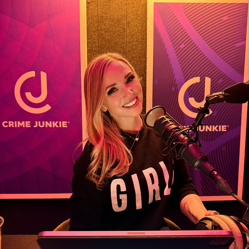 A woman with long blonde hair smiling at the camera, sitting at a desk with a microphone, in a studio with Crime Junkie banners in the background.