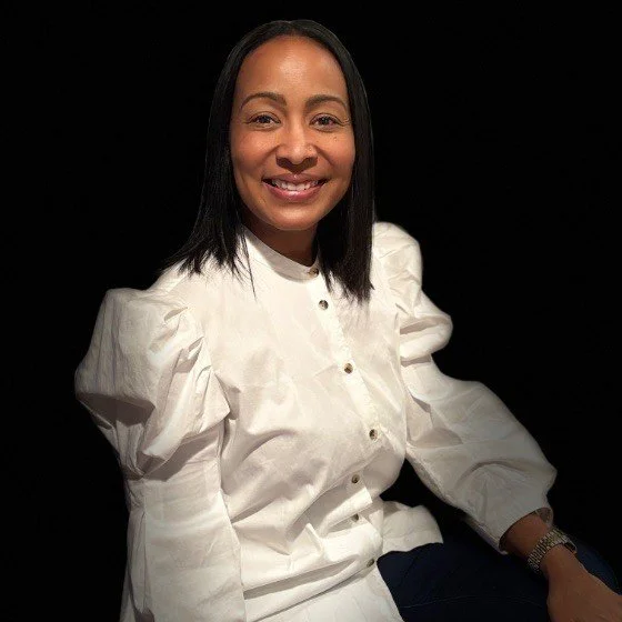 Portrait of a woman with shoulder-length black hair, wearing a white blouse with puffed sleeves, smiling, against a black background.