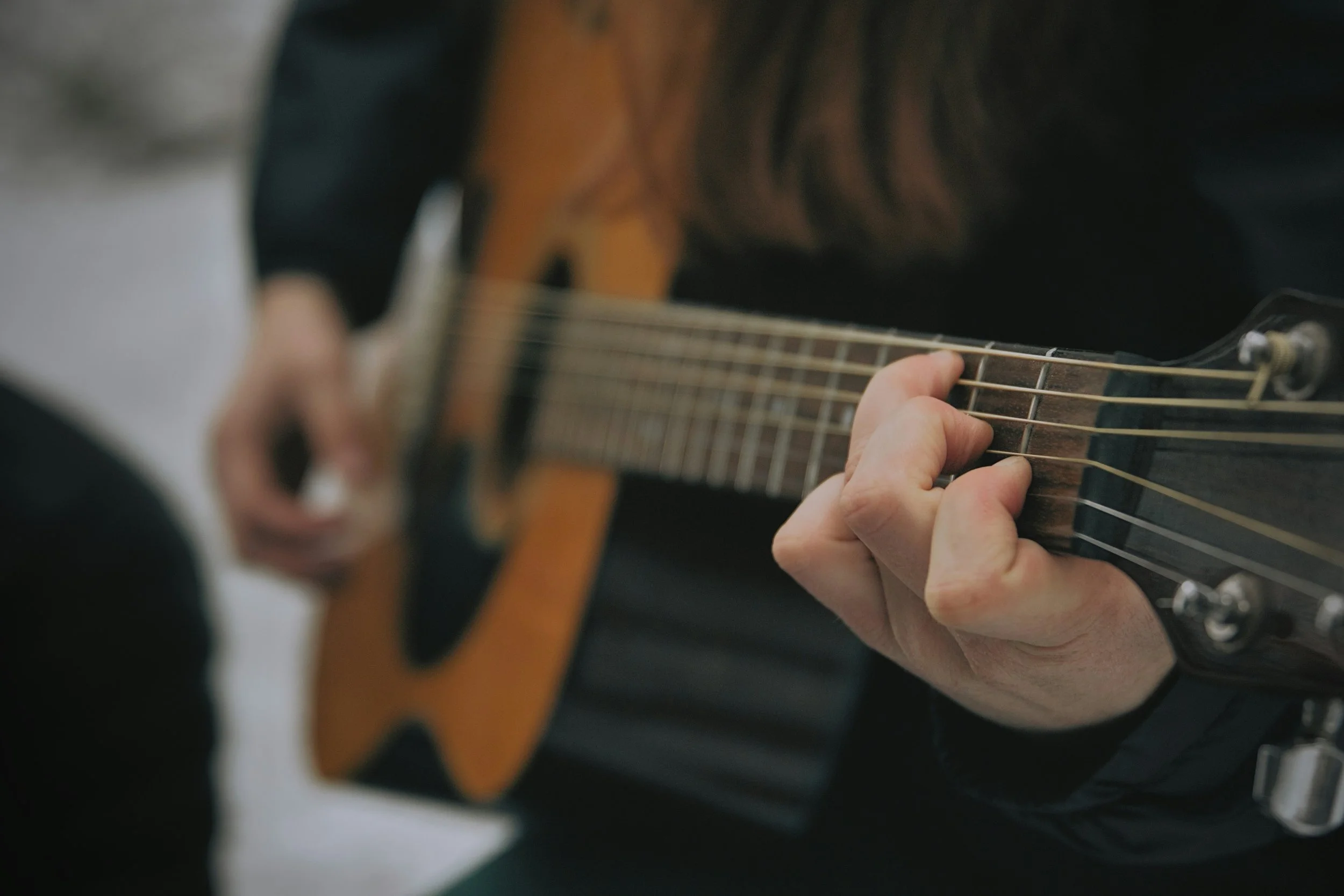 Person playing an acoustic guitar, focusing on their hand on the fretboard.