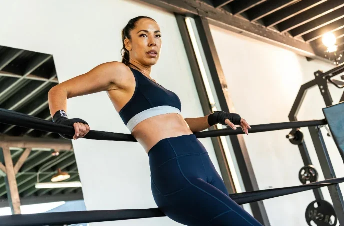 Woman performing triceps dips on gym equipment while wearing navy blue athletic clothing, demonstrating upper body strength and physical fitness.
