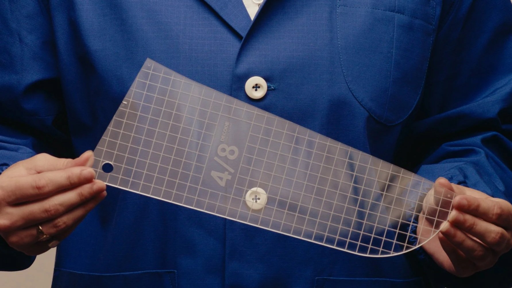 Person in a blue suit holding a clear plastic measurement guide with a label indicating 4/8 inches, two white buttons, and grid lines.