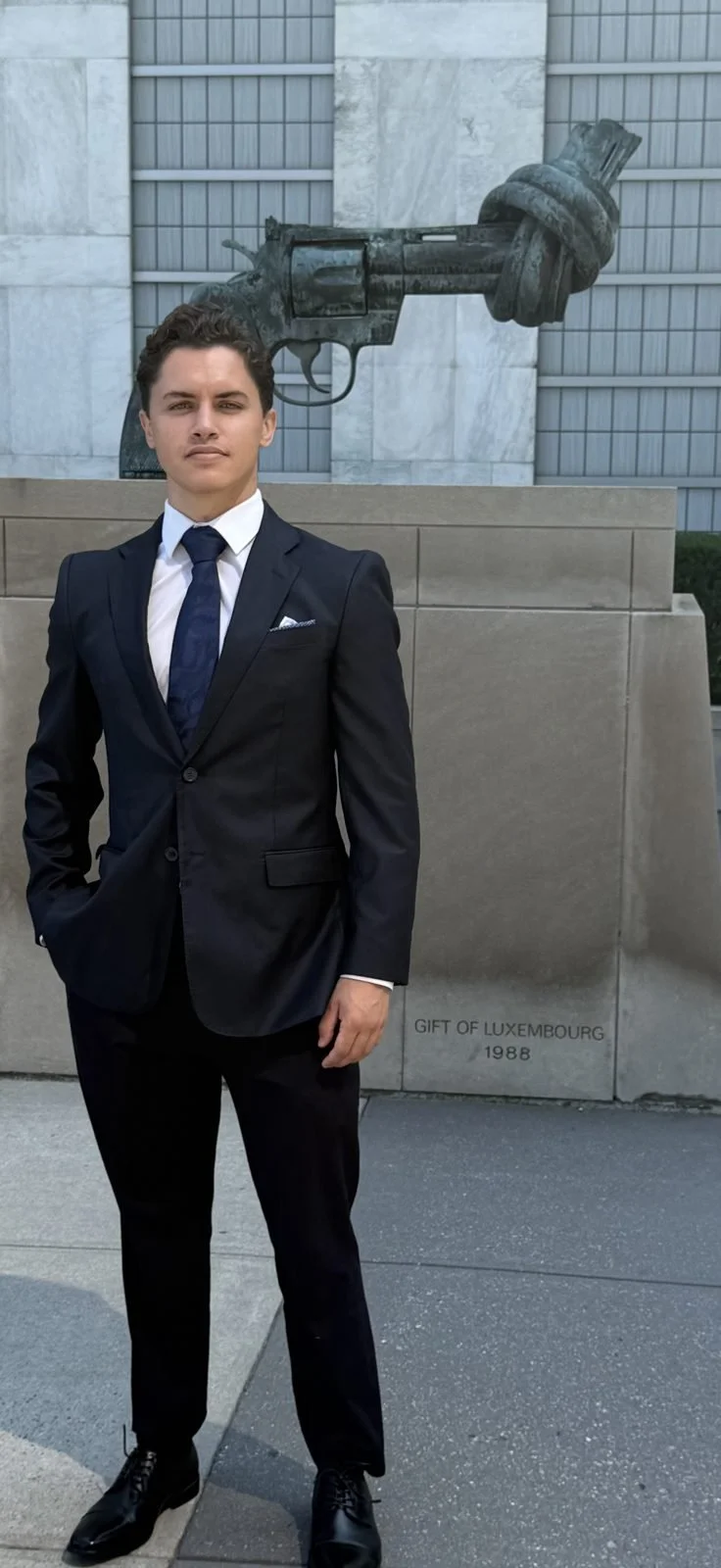 Lucas A. Perry in a black suit and tie beside the Knotted Gun peace sculpture outside the United Nations in New York City.