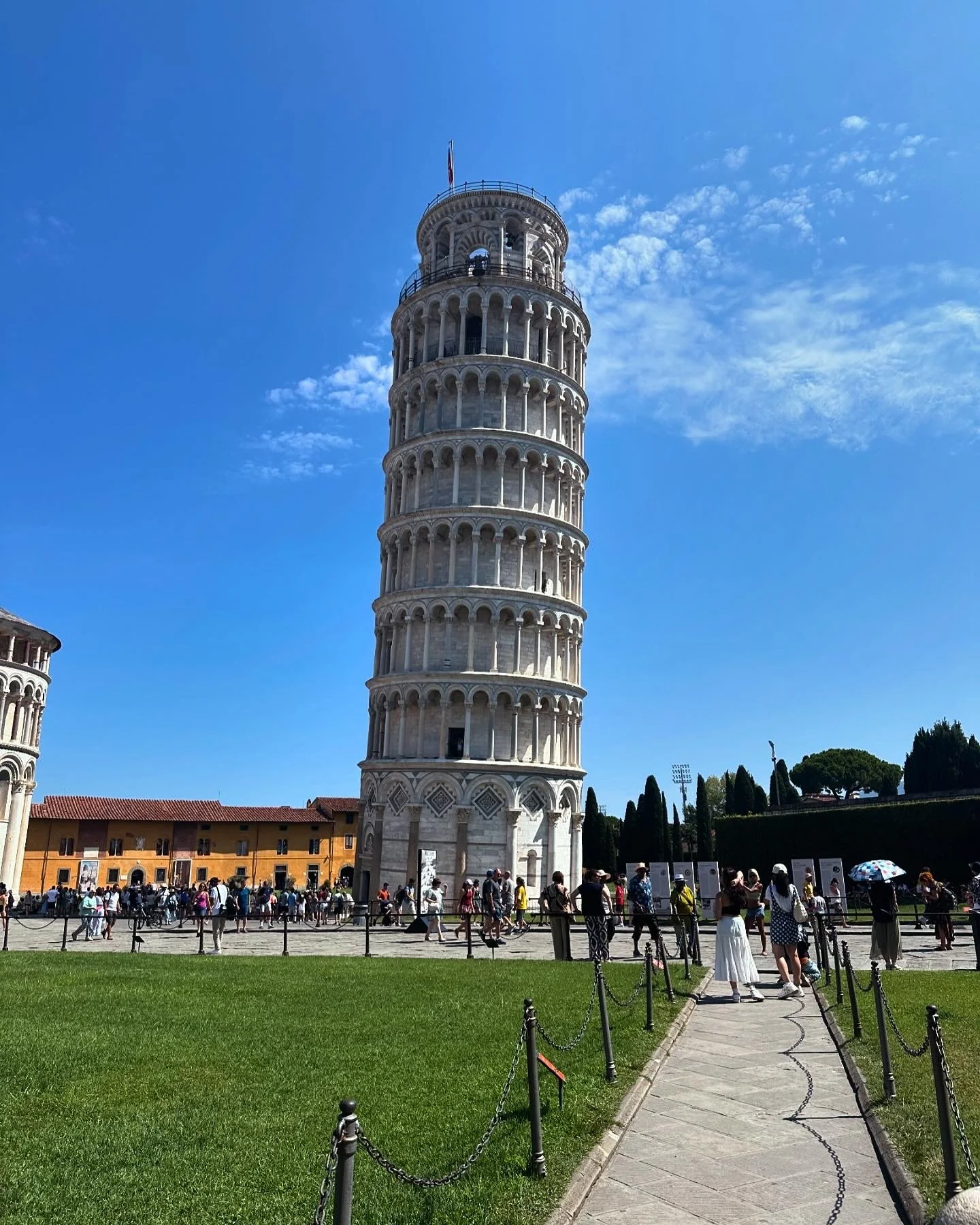 People visiting and taking pictures around the Leaning Tower of Pisa in Italy on a clear, sunny day.