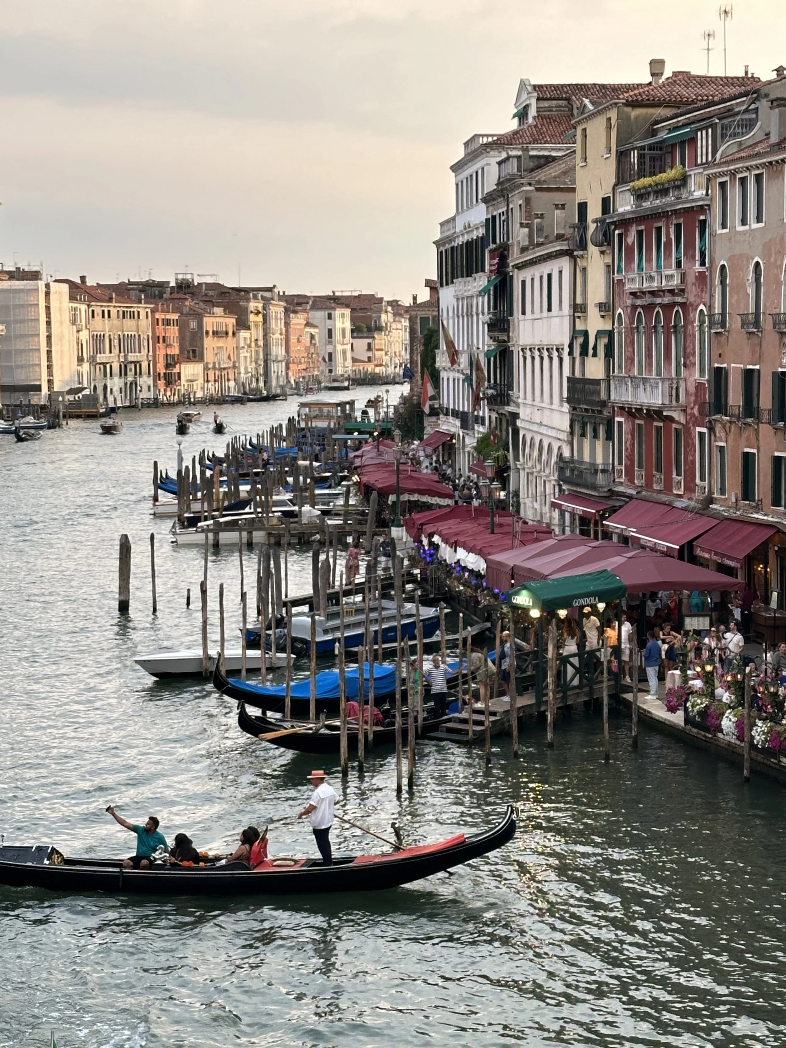 Colorful buildings with outdoor cafes along a canal in Venice, Italy. Gondolas and boats on the water, with people enjoying a boat ride.