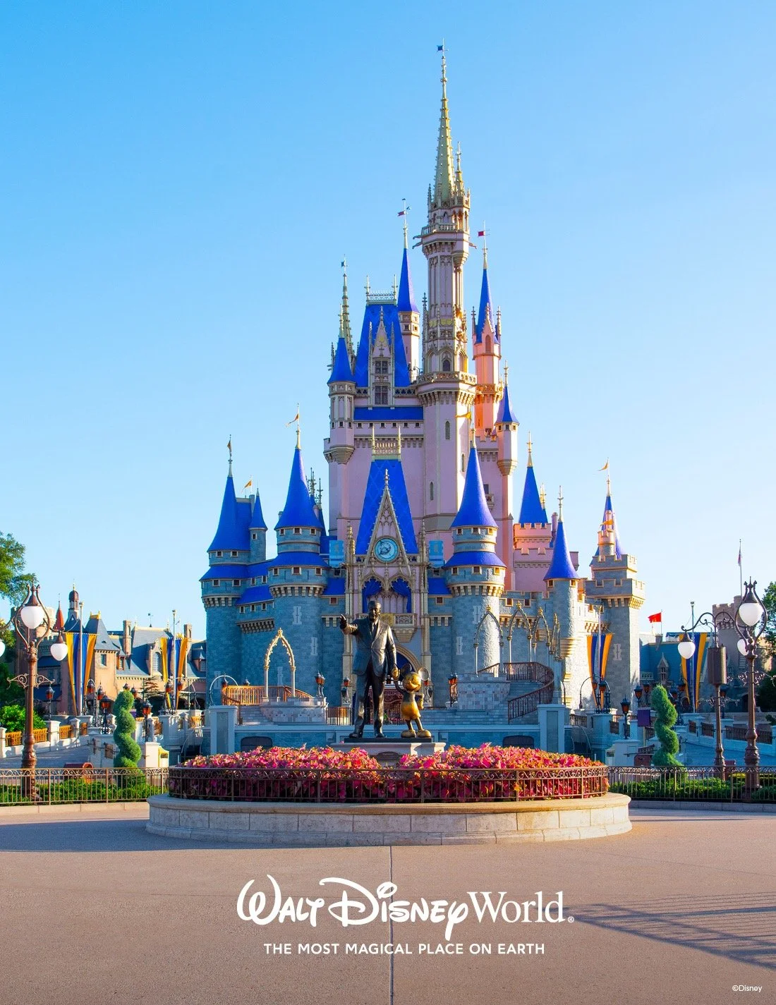 Colorful Cinderella Castle at Walt Disney World with a statue of Walt Disney and Mickey Mouse in front, and floral arrangements around