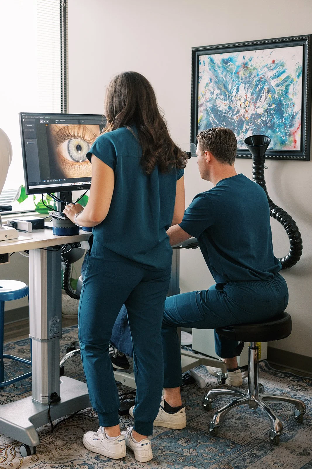 Two medical professionals examining a detailed digital image of a human eye on a computer screen in a clinical setting.