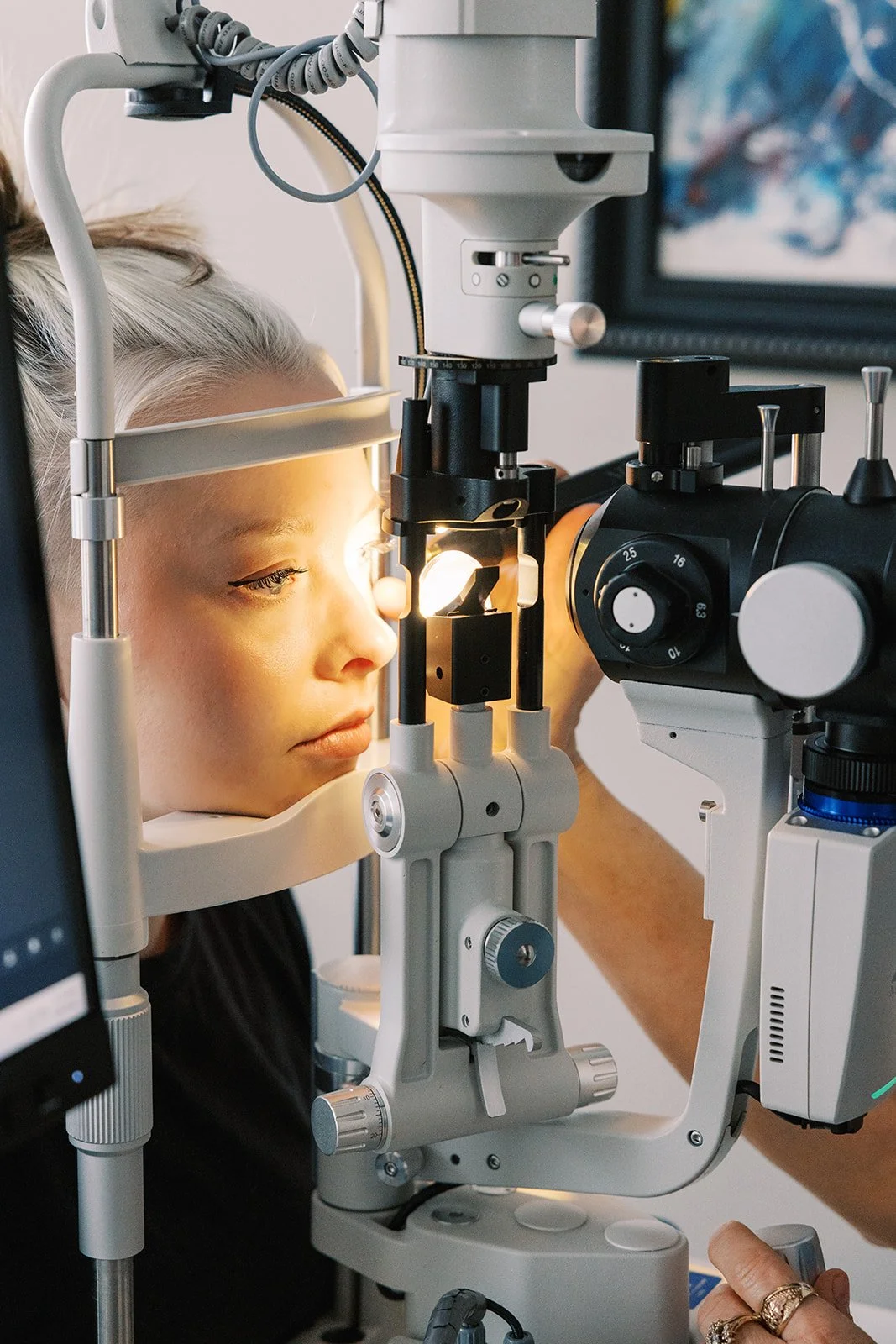 A woman with blonde hair getting her eye examined using a slit lamp during an eye exam.