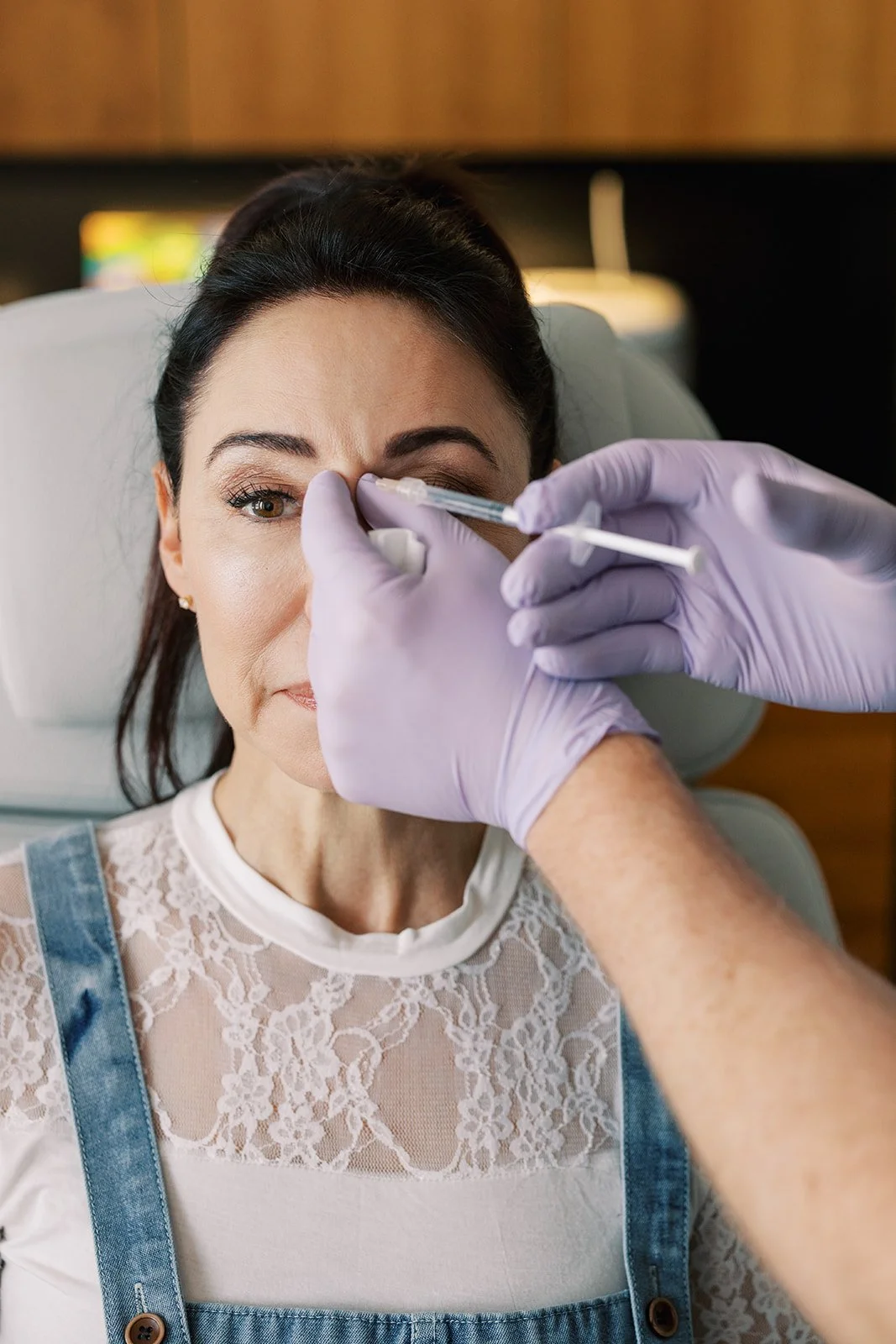 A woman with dark hair getting a cosmetic injection in her forehead from a medical professional wearing purple gloves.