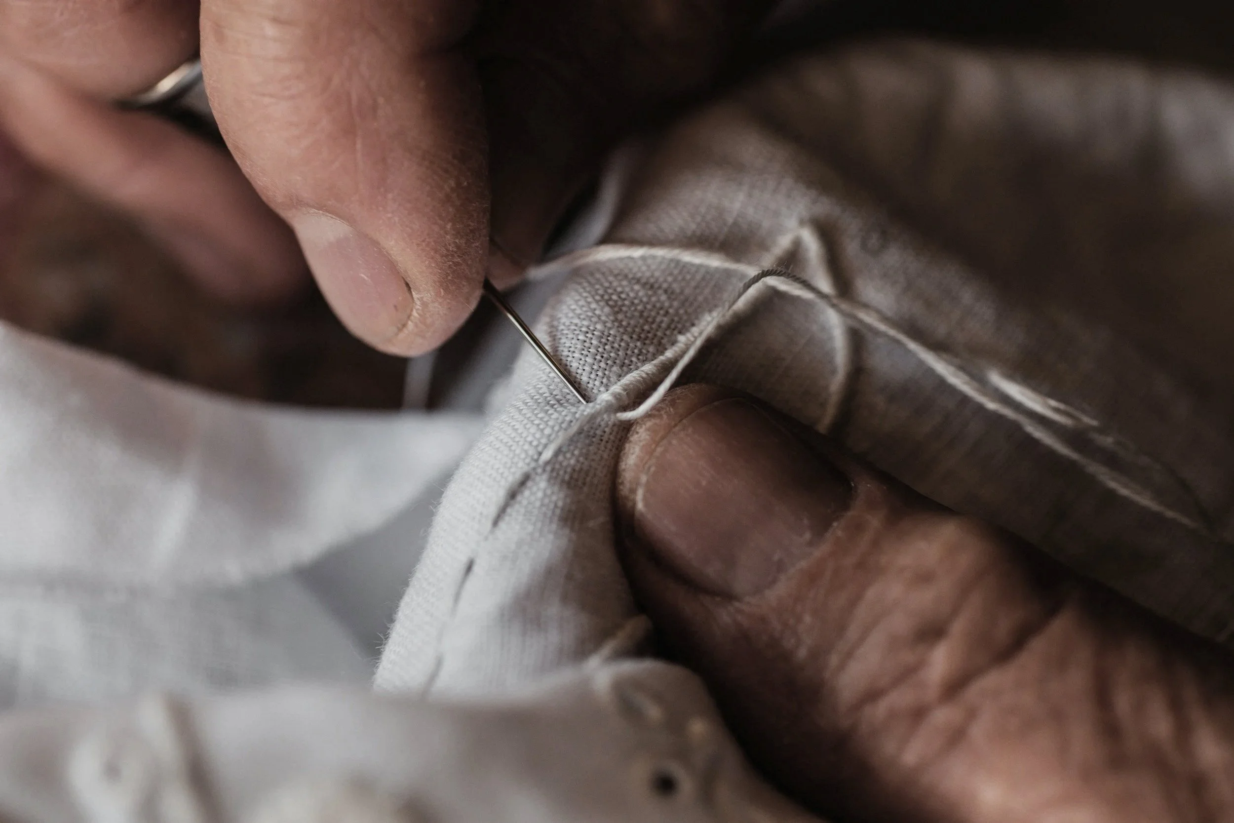 Close-up of a person's hand sewing fabric with a needle and thread.