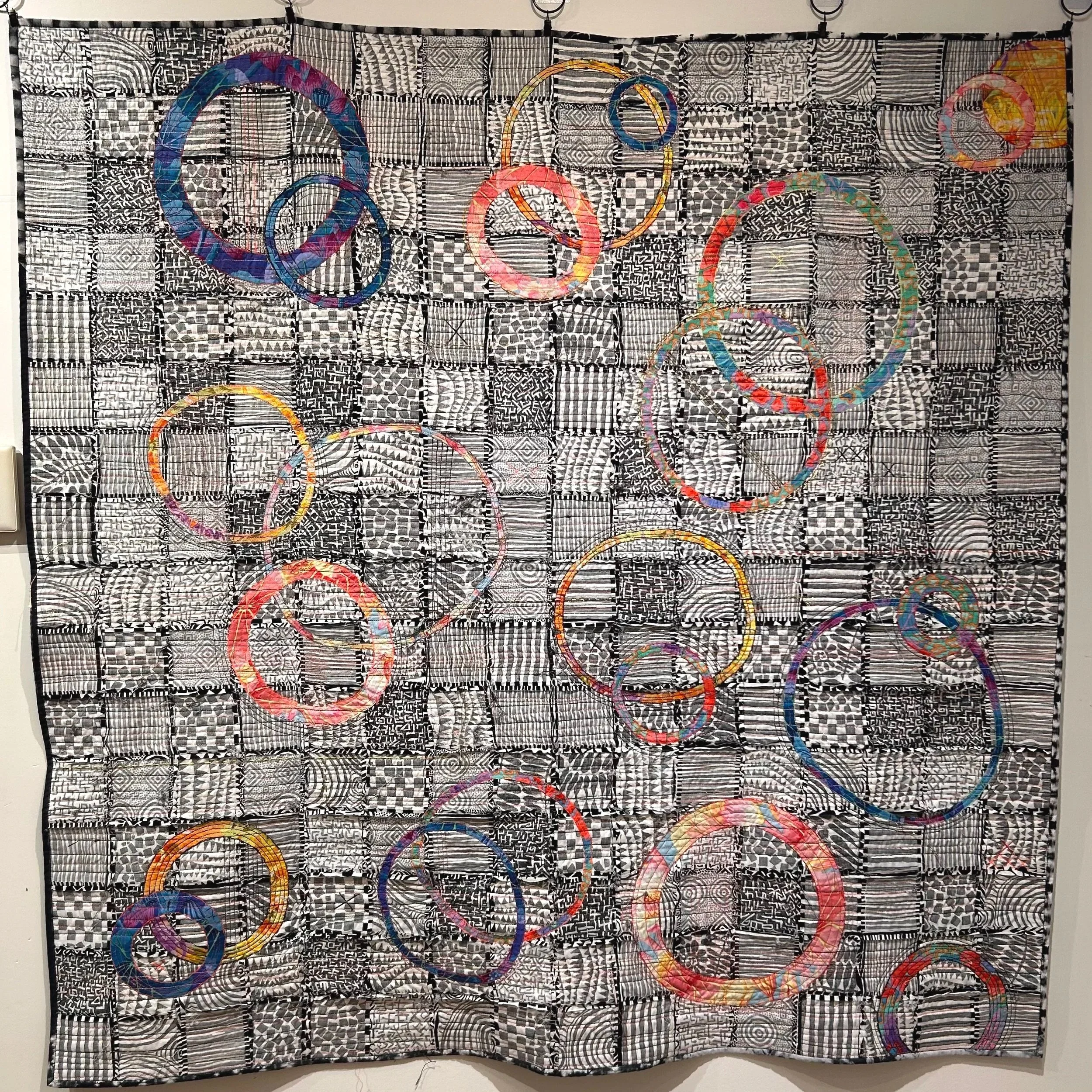 Colorful Olympic rings on a black and white patterned fabric backdrop.