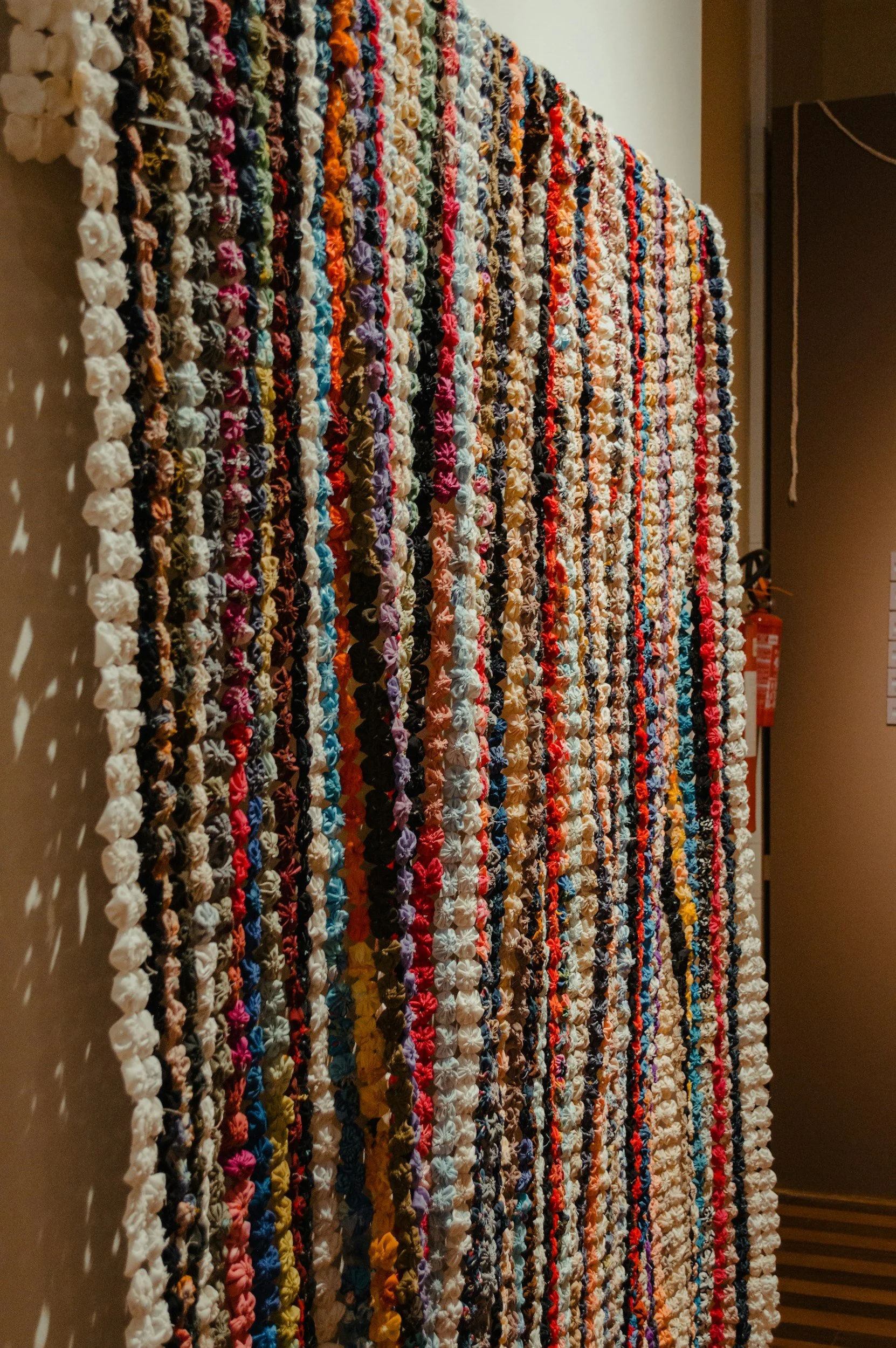 Multi-colored, textured fabric wall hanging with rows of small, gathered fabric pieces in various colors, including white, pink, purple, orange, blue, red, black, and yellow.