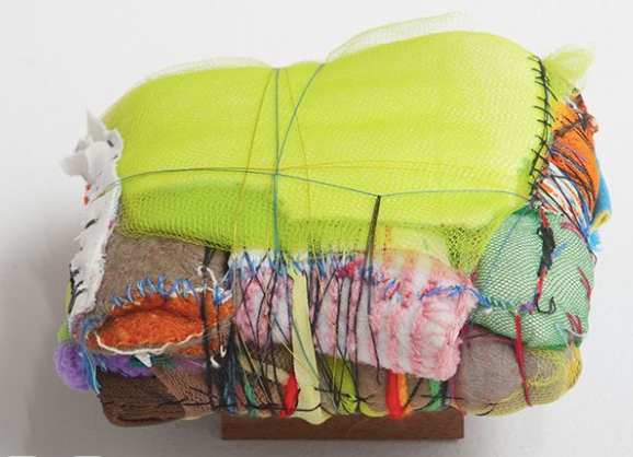 A mixed media art piece featuring a small couch covered with various colorful fabrics, threads, and mesh, with a neon green fabric draped over it.