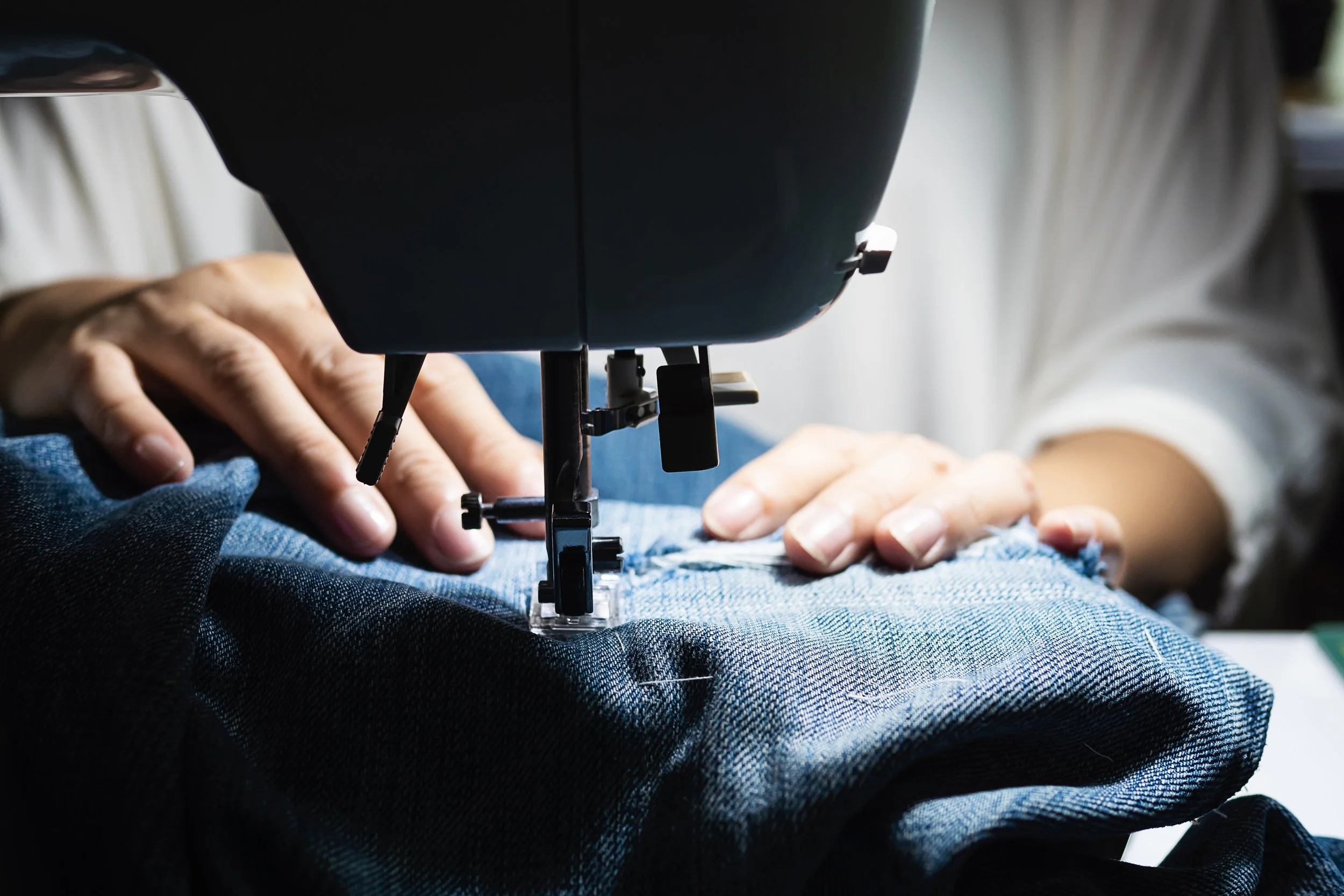 A person sewing denim fabric using a sewing machine.