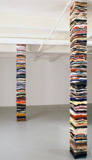 Two tall columns made of stacked, colorful fabric or paper strips in a gallery or installation space.