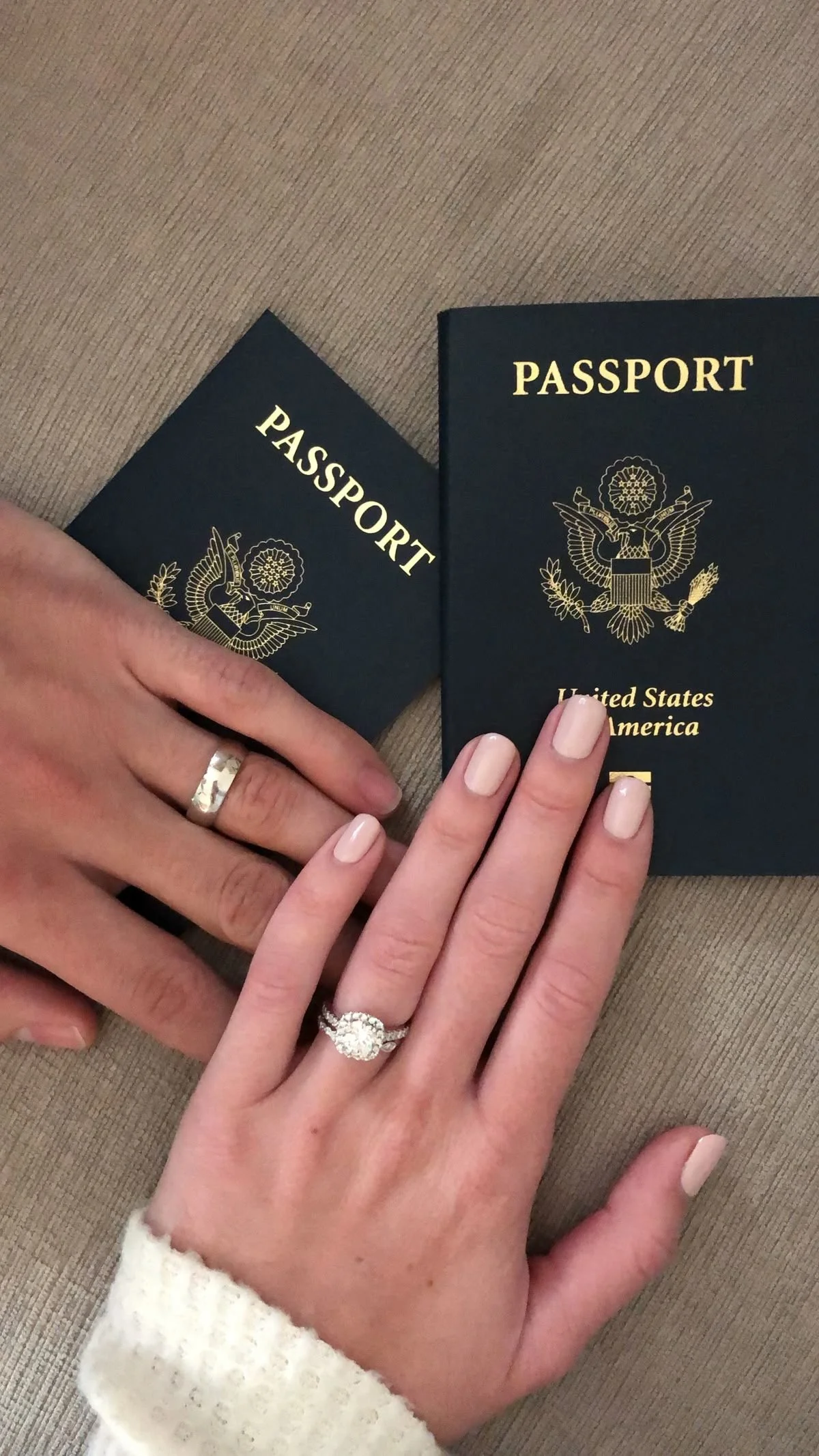 A person with a wedding ring has their hand resting on a surface near two U.S. passports.